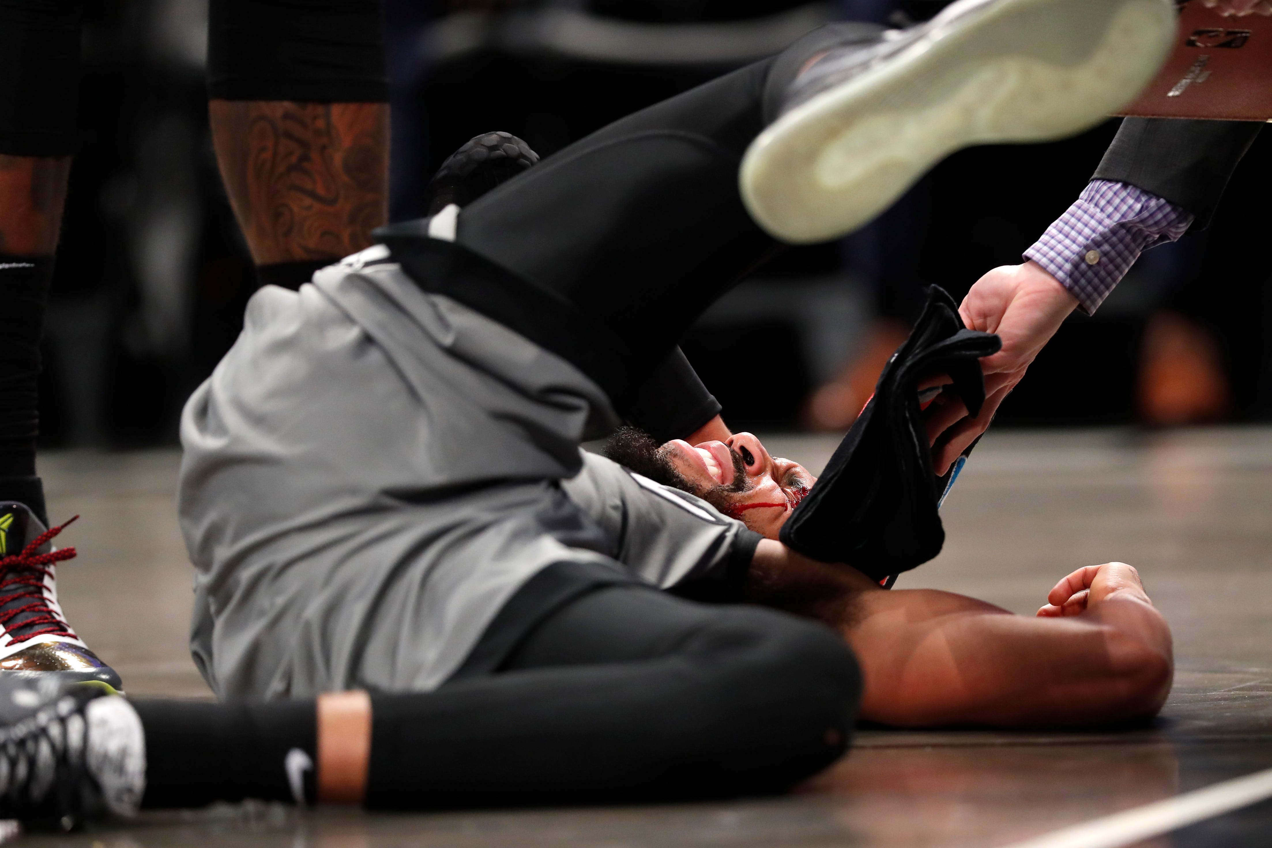 An assistant hands a towel to Brooklyn Nets guard Garrett Temple, who lies on the floor after he was hit in the face during the first half.