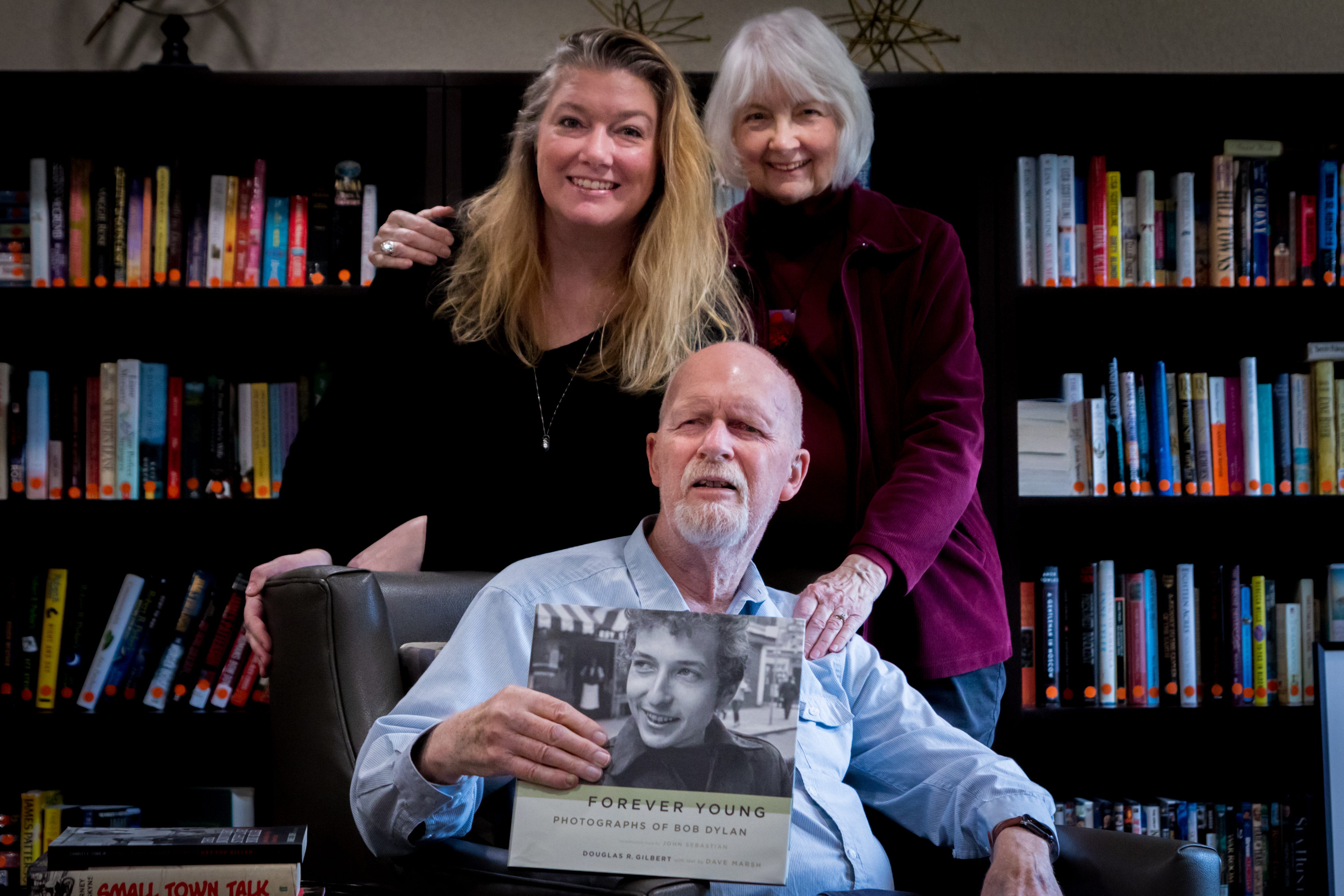 Photographer Douglas R. Gilbert poses with daughter Anne Carpenter and wife Barbara Gilbert, while displaying a book of his photographs of a young Bob Dylan from 1964.
