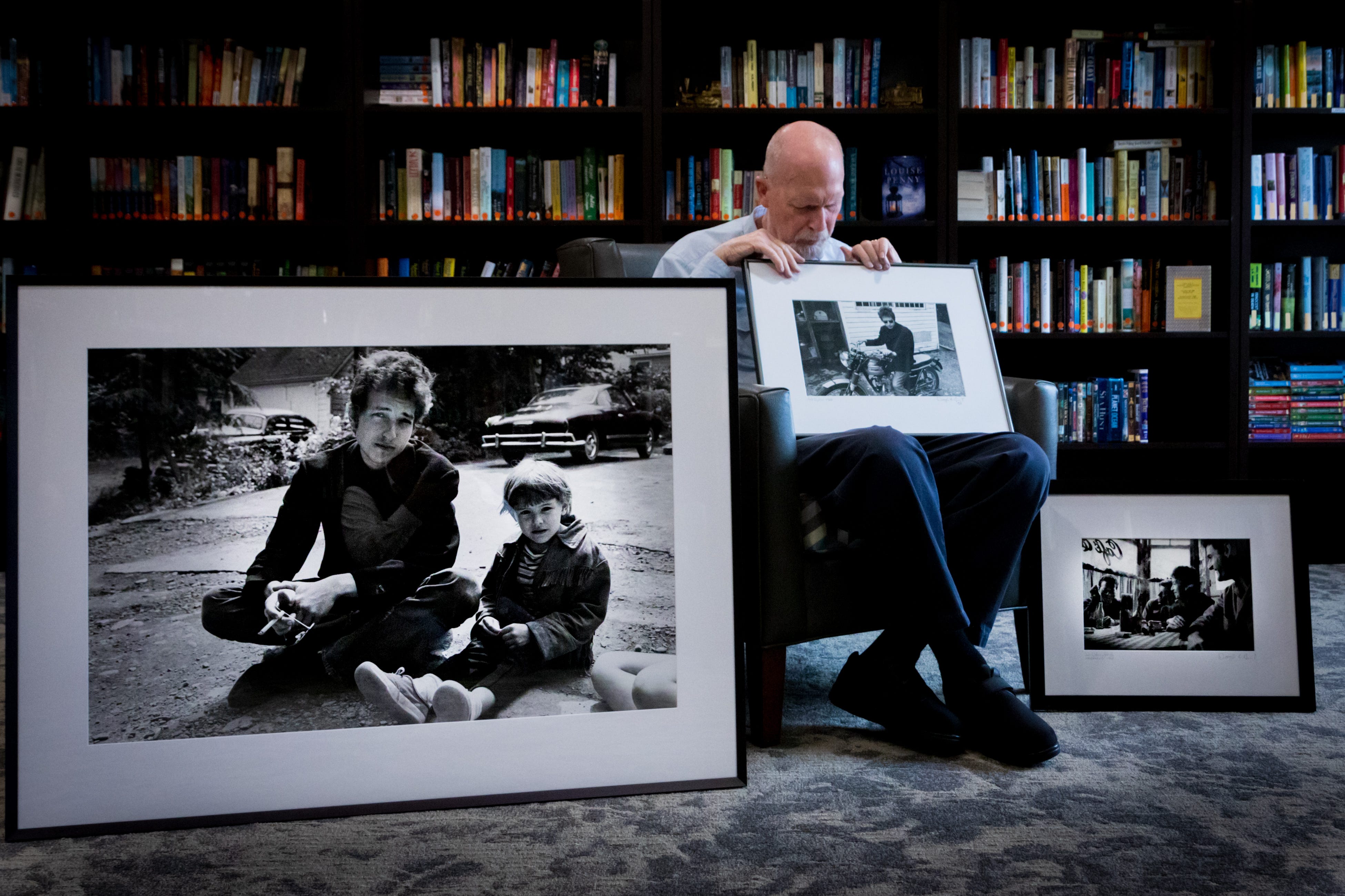 Douglas R. Gilbert displays photographs he made of Bob Dylan back in 1964. The large photo in front is of Bob Dylan behind the Cafe Espresso in Woodstock, NY with the daughter of Bernard and Mary Lou Paturel (owners of the cafe). The photo being held is Bob Dylan on a Triumph, behind Cafe Espresso, Woodstock, NY. The photo on the far right is (left to right) Mason Hoffenberg, John Sebastian, Bob Dylan and Victor Maymudes at Cafe Espresso, Woodstock, NY.