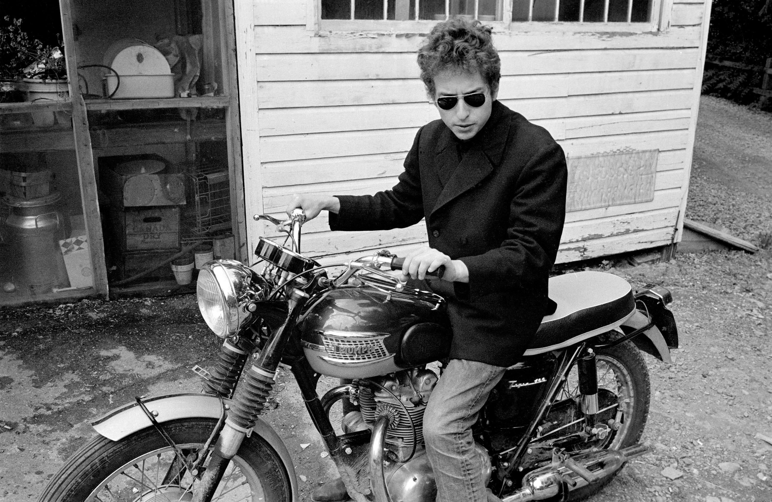 Bob Dylan astride his Triumph motorcycle in Woodstock, New York. (1964)