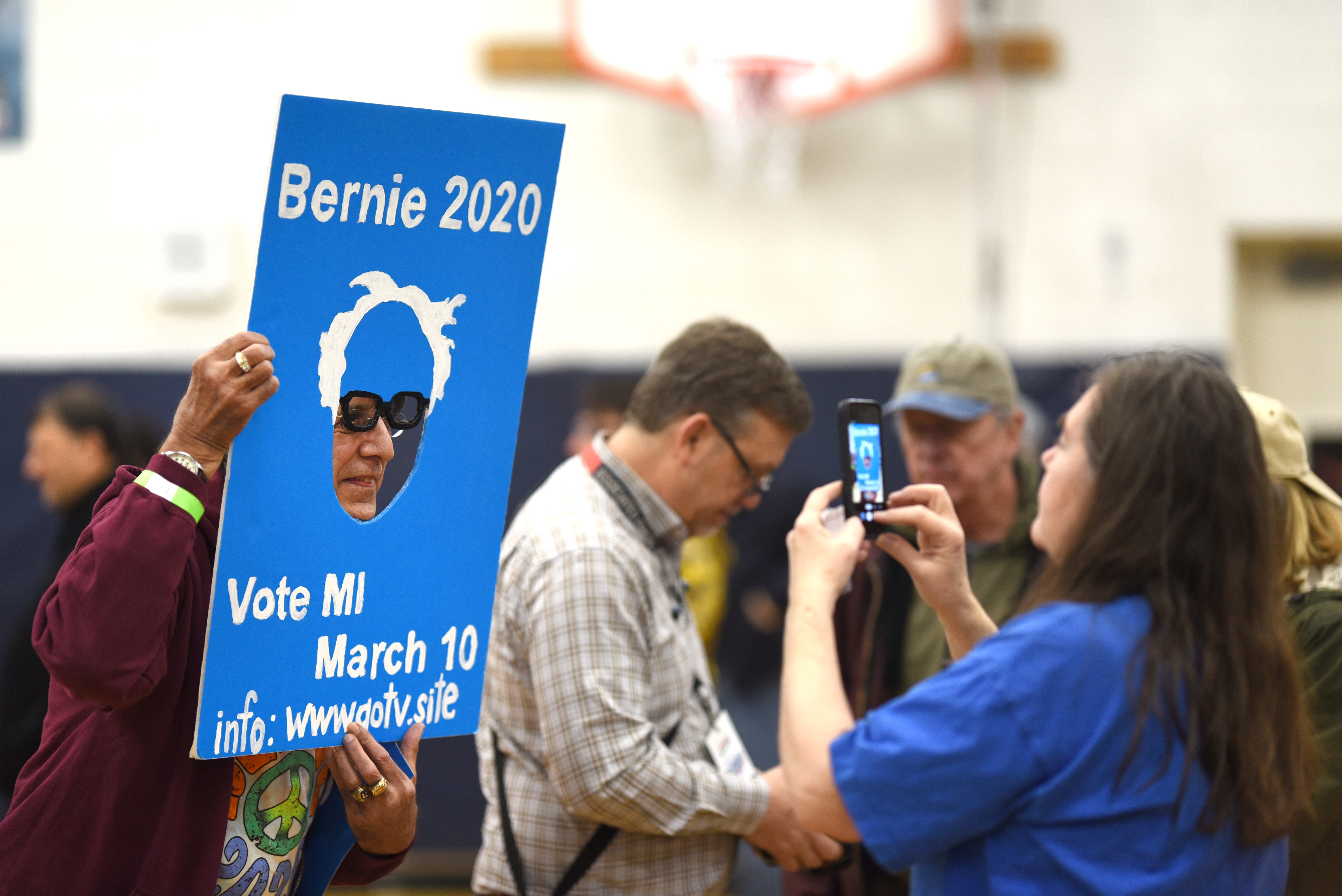 Joseph Borrajo, left, of Dearborn peers through a get out the vote poster during a Bernie Sanders campaign stop.
