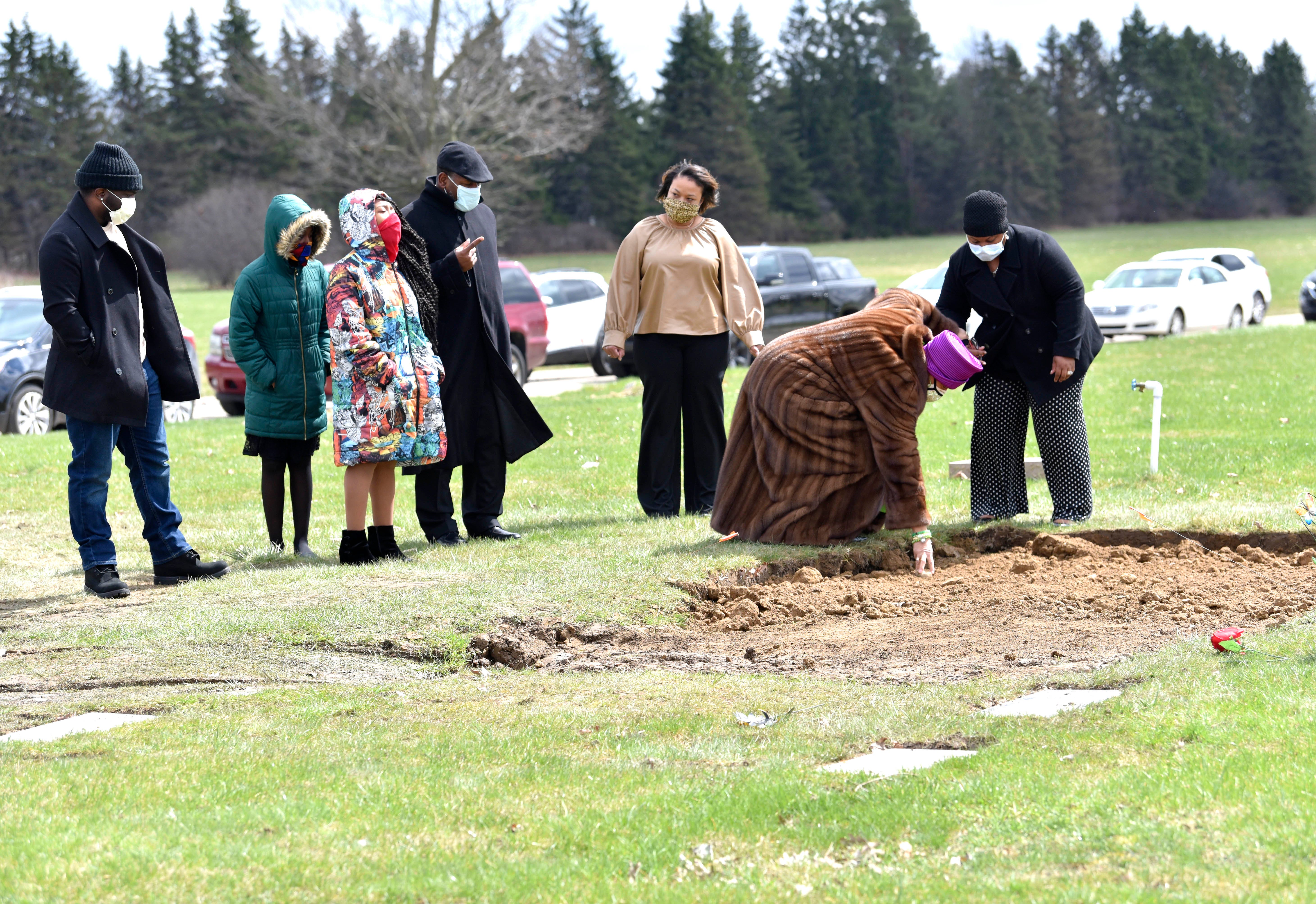 Sandy Brown bends over to pick up a rock from the gravesite of her son, Freddie Lee Brown III, and her husband, Freddie Lee Brown Jr., whie others pay respects from their vehicle.