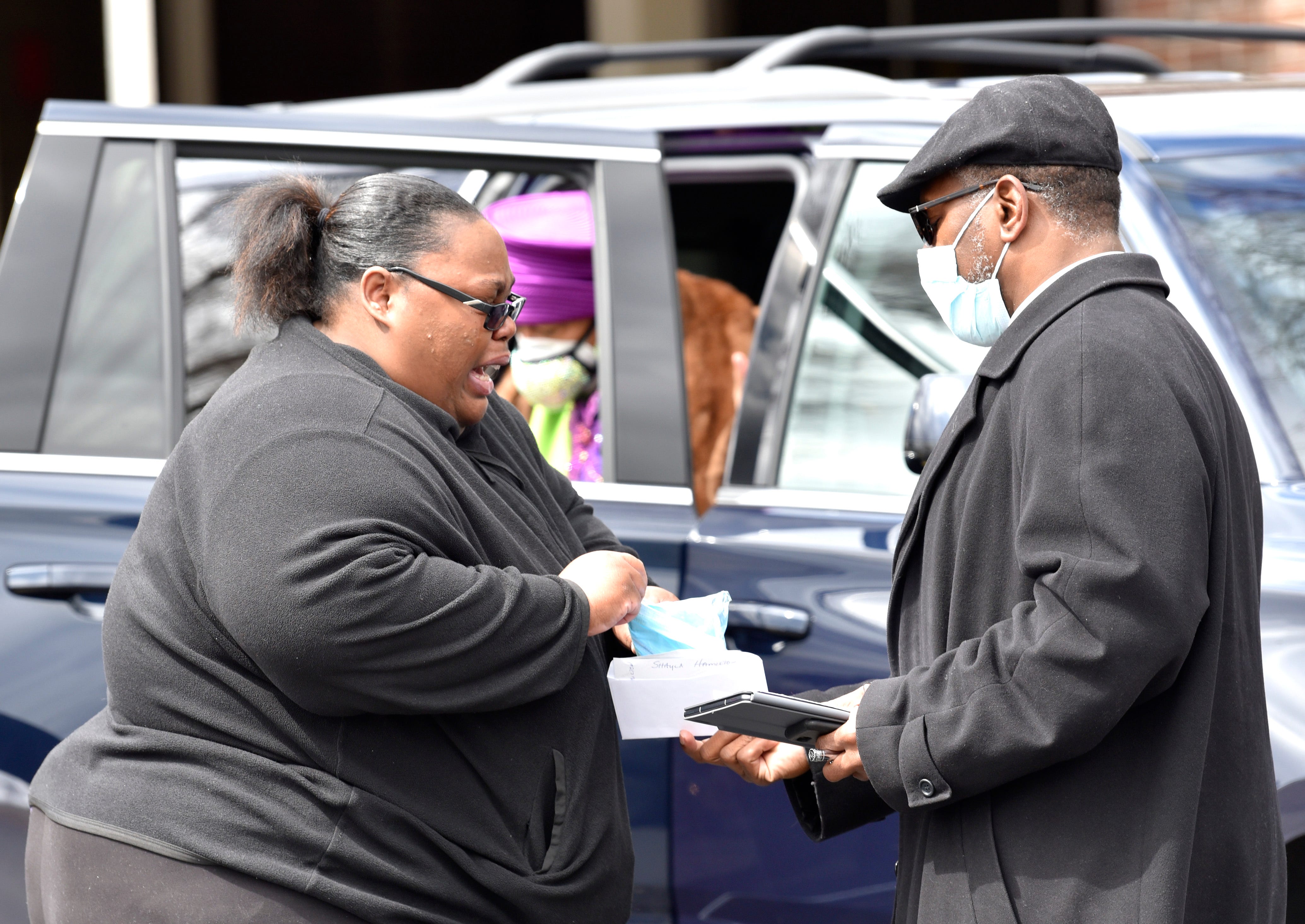 Shayla Hamilton, left, of Grand Blanc, wails as Jackson Memorial Temple Church of God in Christ Pastor Kiemba Knowlin hands her a face mask before she enters the funeral home. She is niece to Brown Jr. and cousin of Brown III.