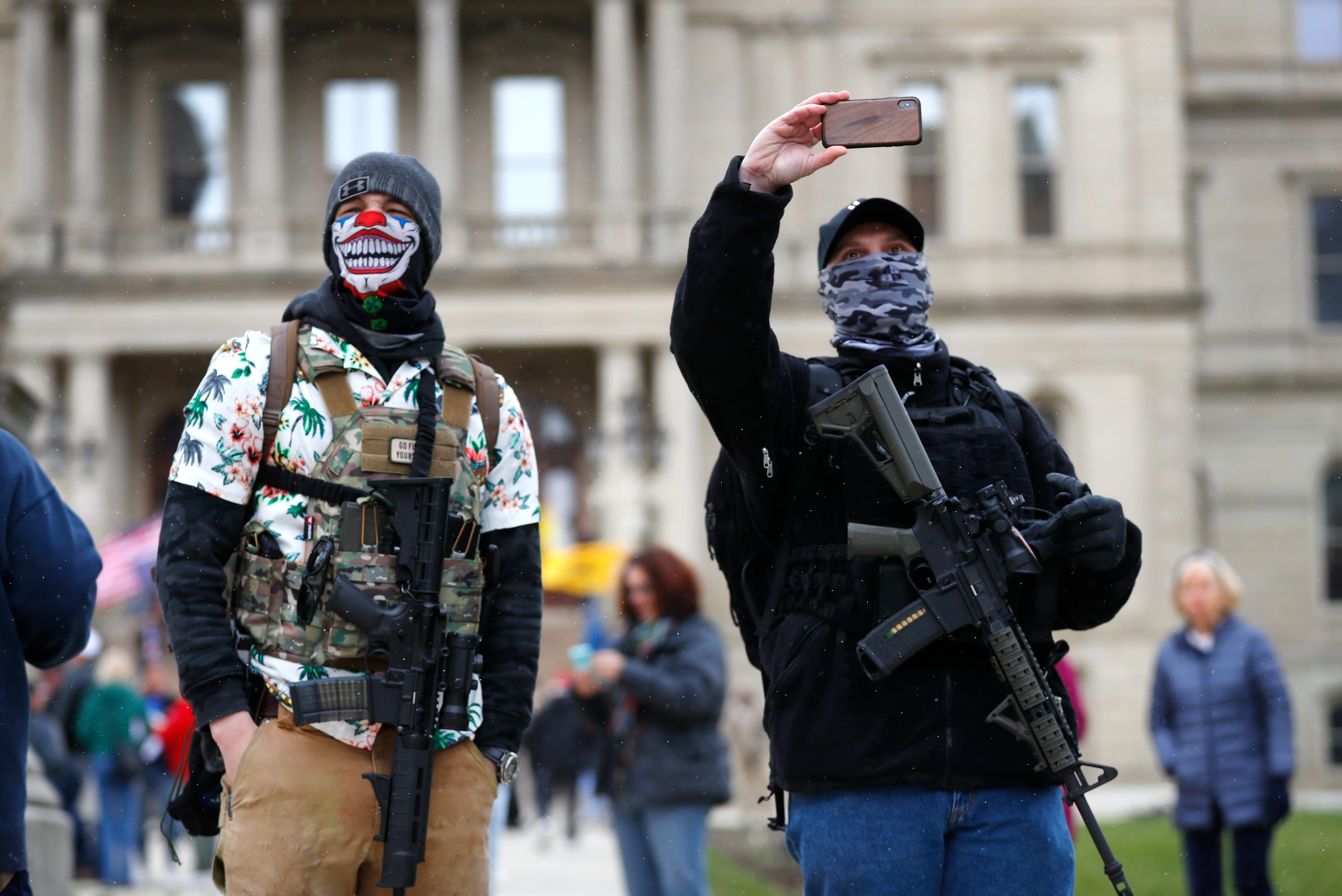 People with rifles watch outside the state Capitol in Lansing on Wednesday, April 15, 2020, to protest Gov. Gretchen Whitmer ' s orders to keep people at home and businesses locked during the COVID-19 outbreak