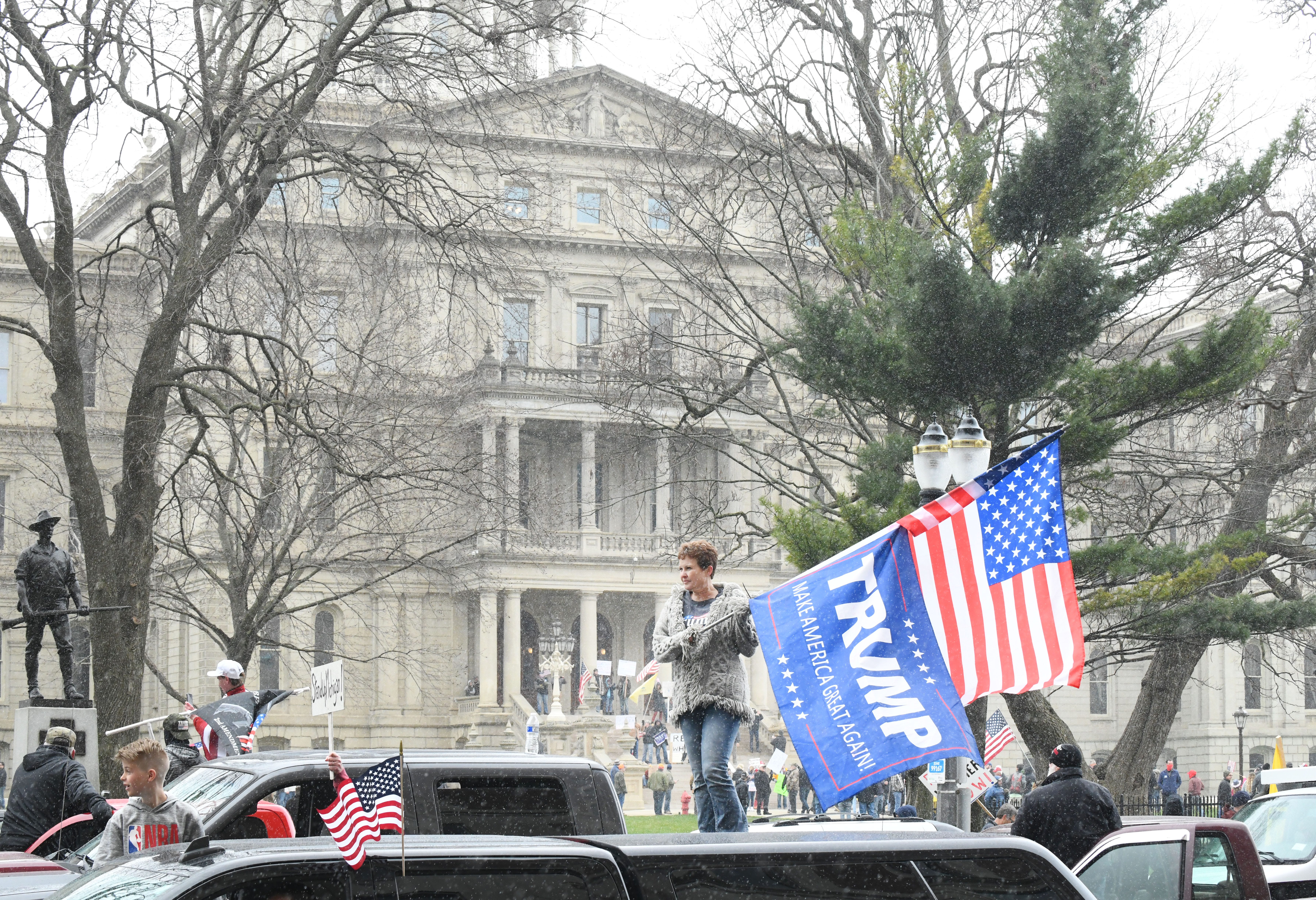 Deborah Creque waves American and Donald Trump flags as she and other protesters surround the state Capitol during Operation Gridlock in Lansing on April 15, 2020.