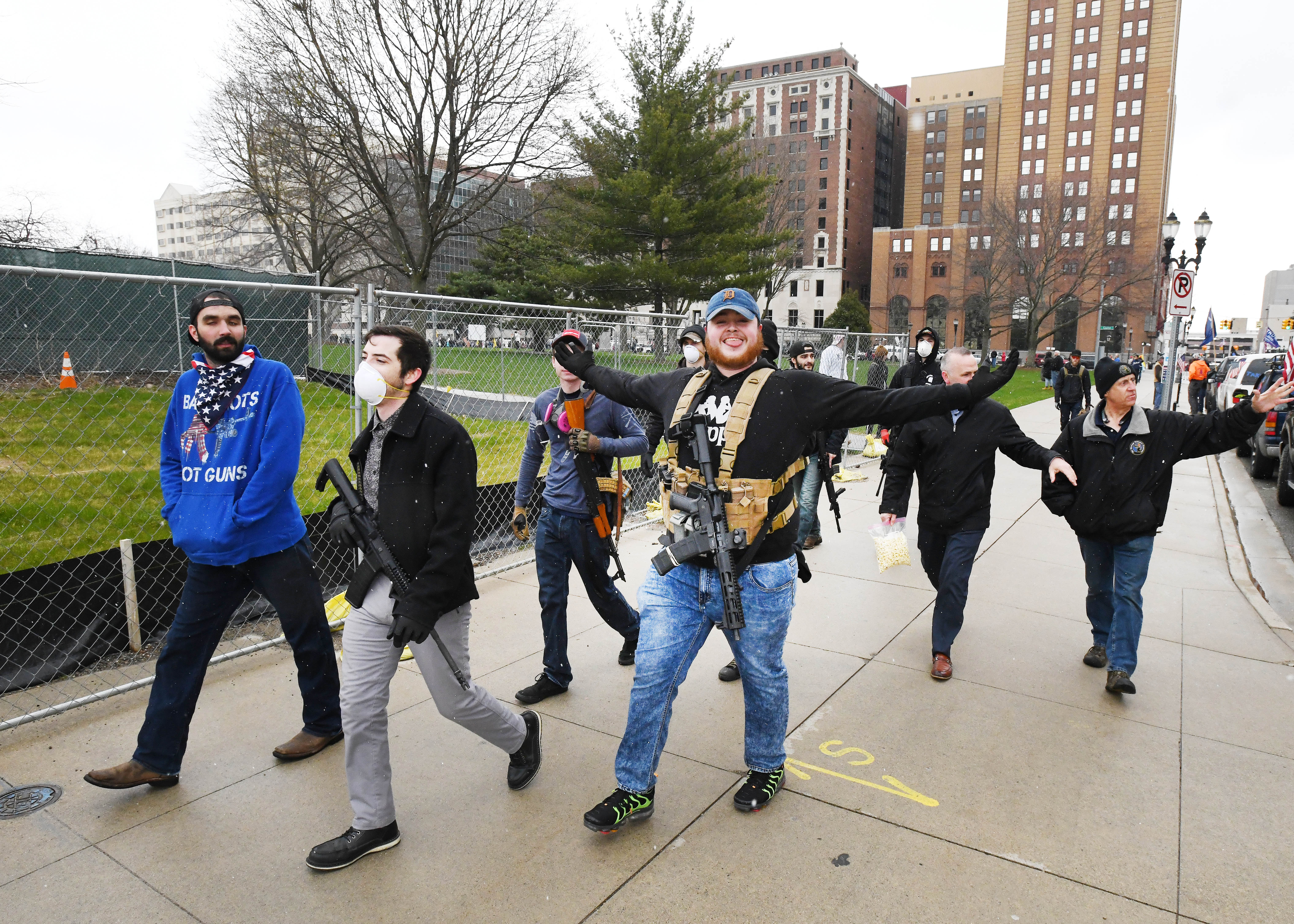 A group of protesters carrying weapons walks along West Allegan Street past the Capitol.