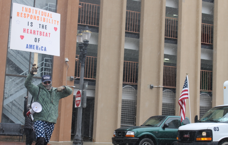 An unnamed protester crosses the street during a demonstration against Gov. Gretchen Whitmer's stay-at-home order on Wednesday, April 15, 2020.