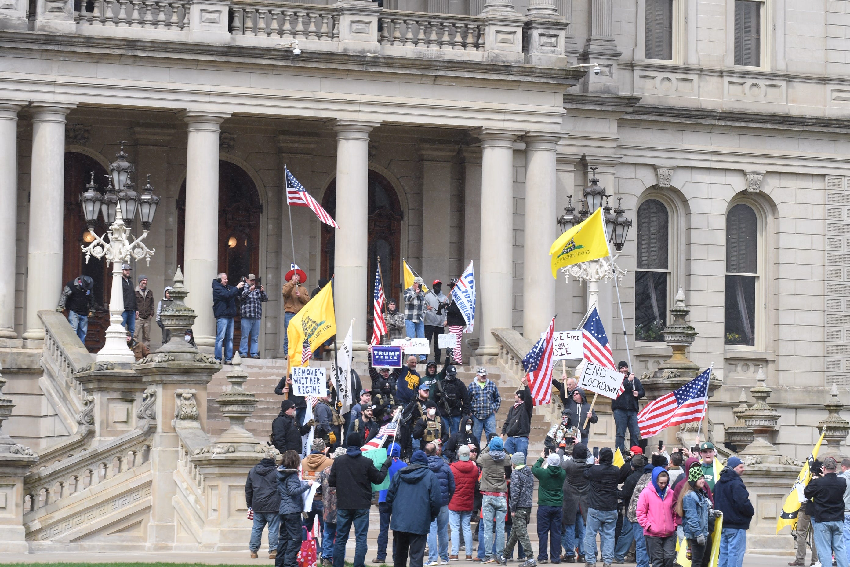 Individuals protesting Gov. Gretchen Whitmer ' s stay-home order gather, waving flags and signs against the safety measures intended to stop the spread of coronavirus on the front steps of the Capitol in Lansing on Wednesday, April 15, 2020.