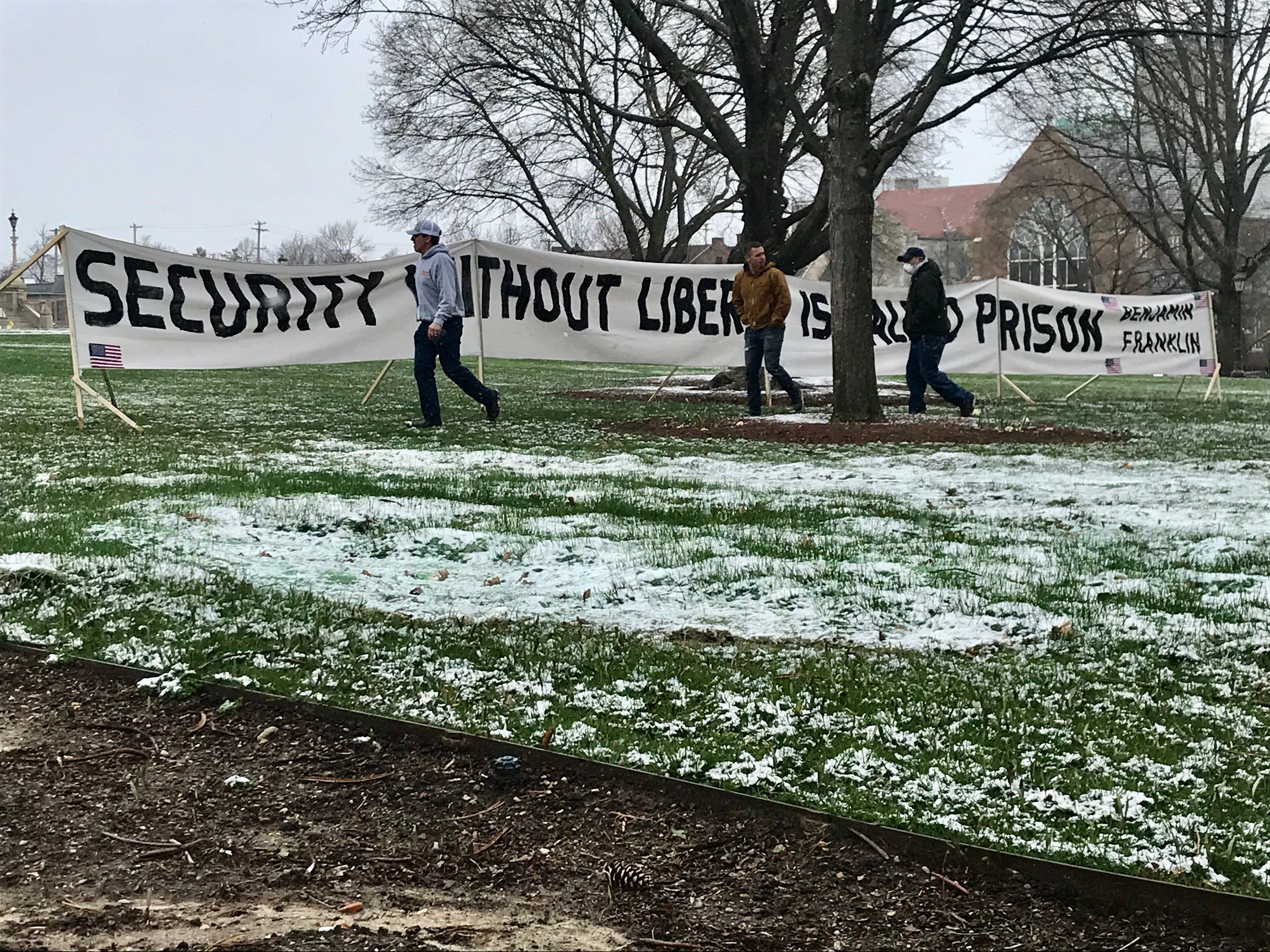 Protesters stand in front of a sign on the Capitol lawn on Wednesday, April 15, 2020. The event is a demonstration against restrictions imposed by Gov. Gretchen  Whitmer's stay-at-home order.