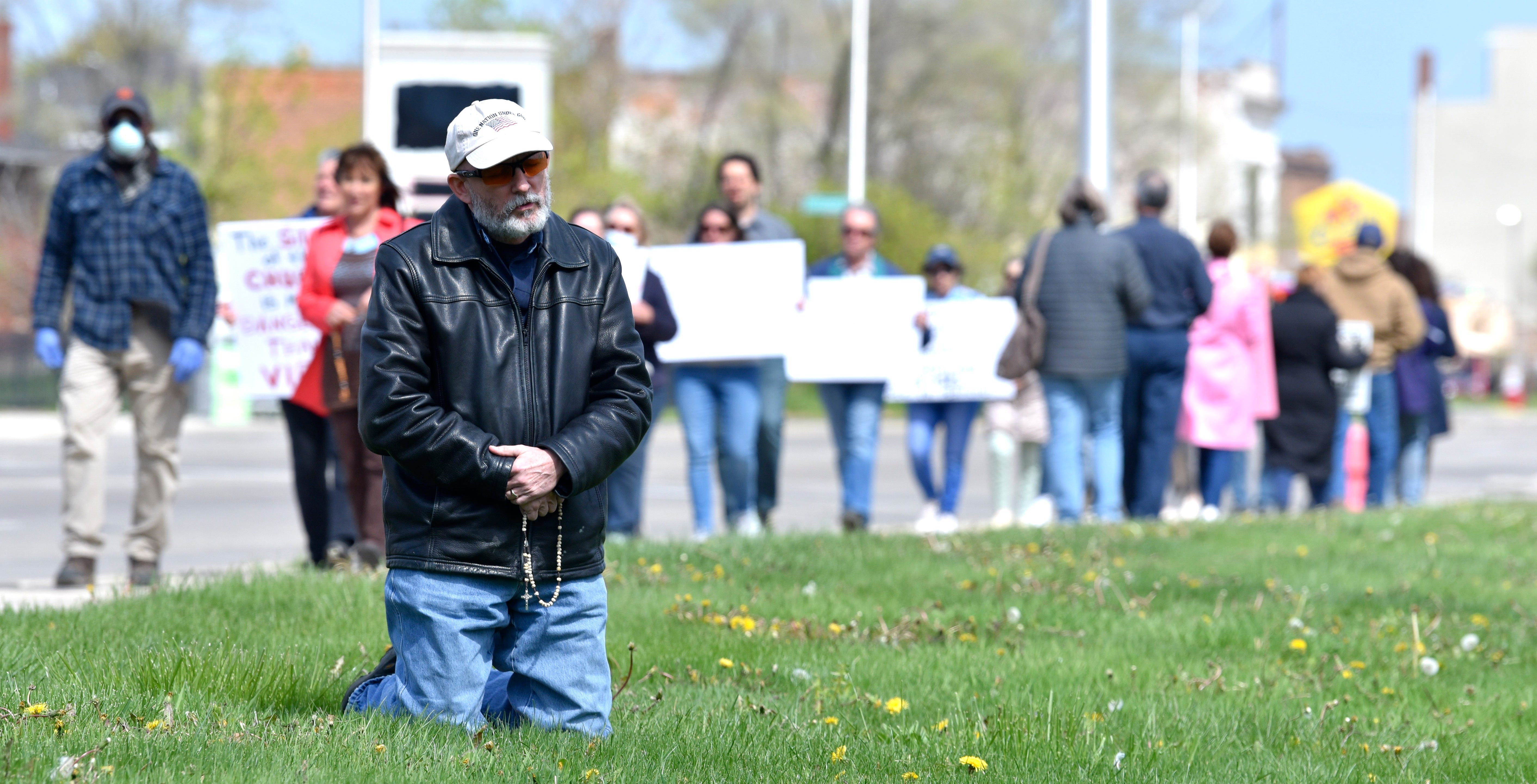 Barry Doherty, of Ortonville, kneels as he Prays the Rosary as more than 50 believers gather in front of the Cathedral of the Most Blessed Sacrament on Woodward Ave. in Detroit, Thursday morning, May 7, 2020, to demand that Arch Bishop Allen Vigneron reopen Catholic churches that have been closed since March because of COVID-19.