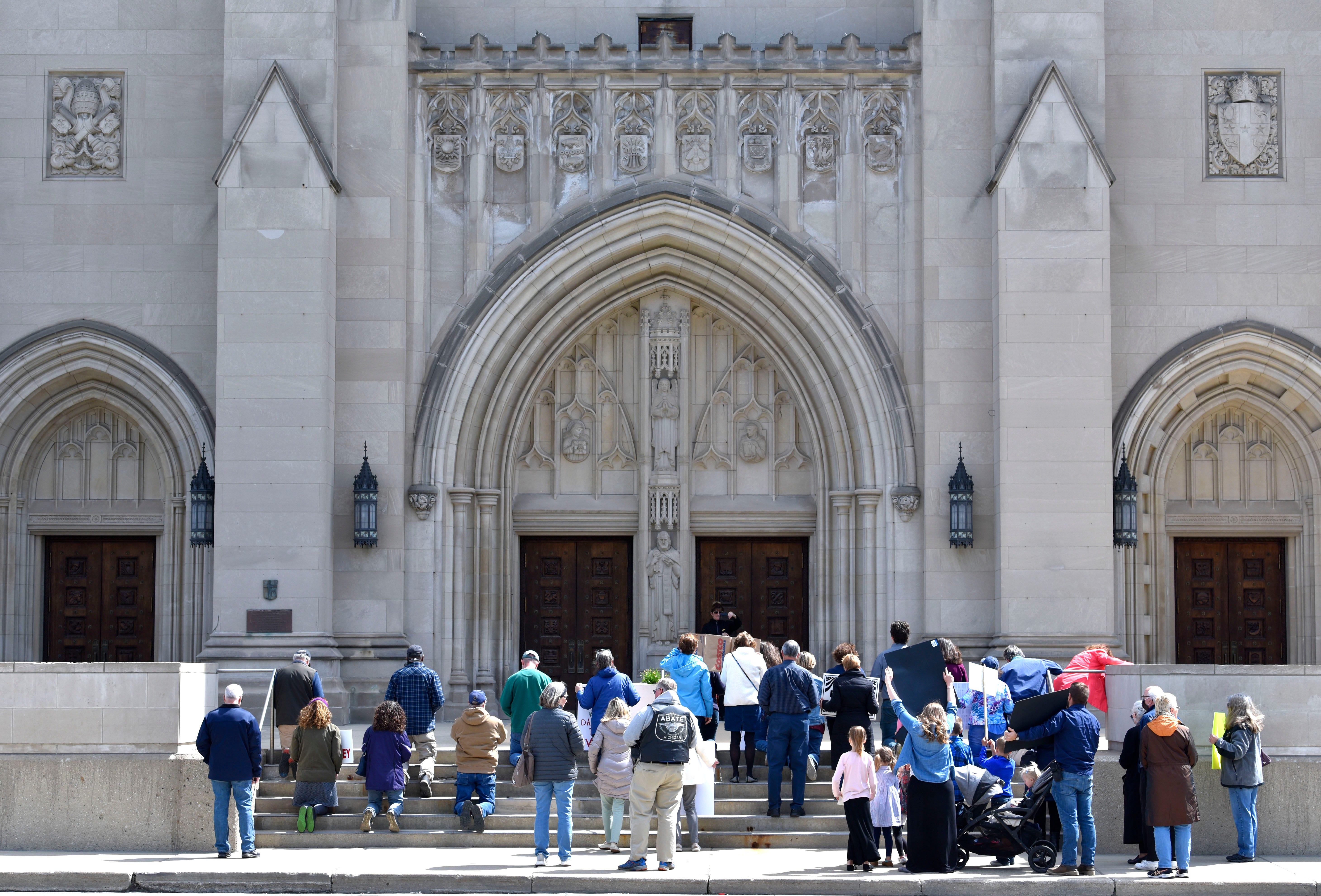Believers kneel and stand in front of the Cathedral of the Most Blessed Sacrament to demand that Arch Bishop Allen Vigneron reopen Catholic churches that have been closed since March because of COVID-19.