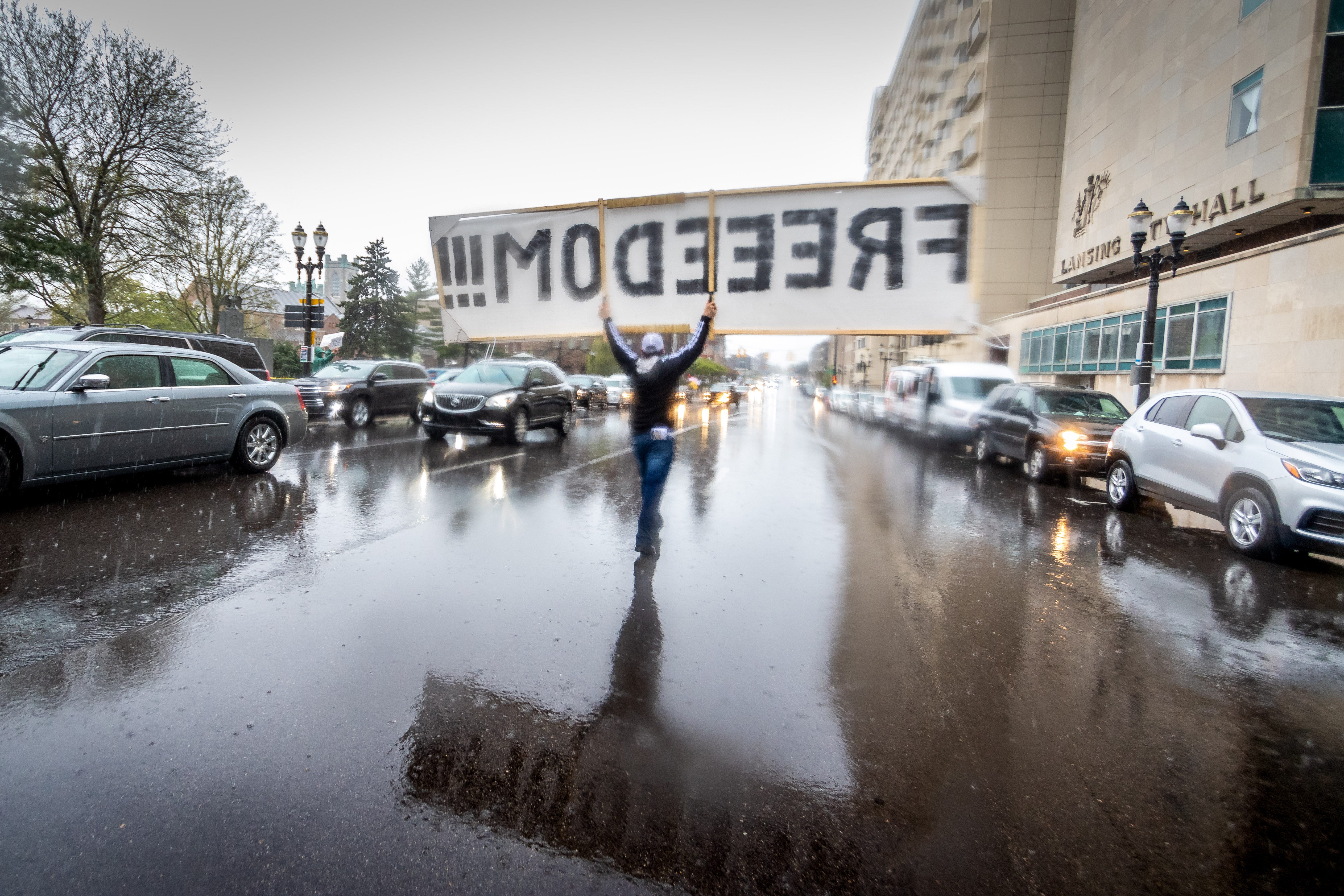 An unknown protestor carries a sign down a Lansing street in front of the state Capitol.