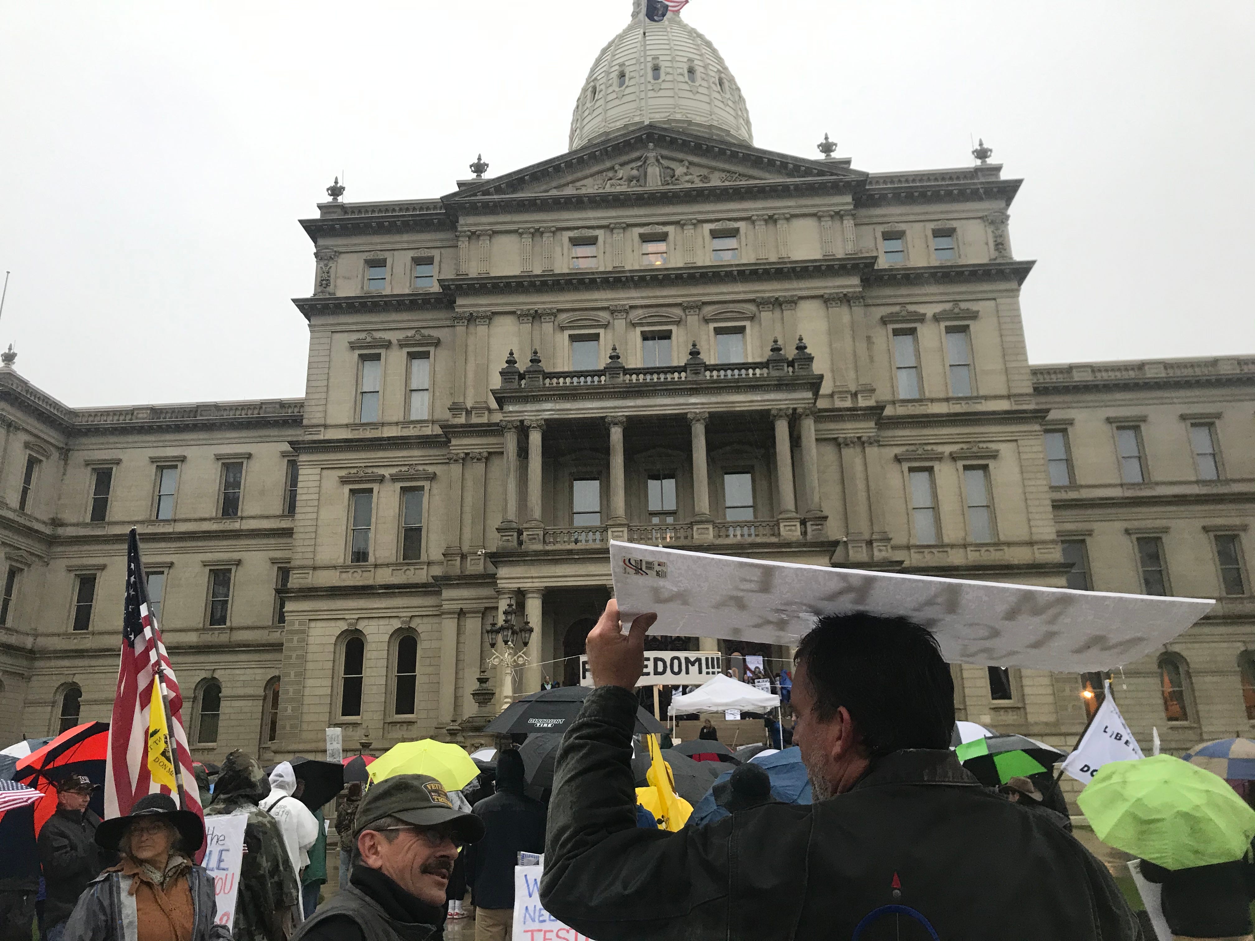 A participant in a protest at the Michigan Capitol on Thursday, May 14, 2020, uses his sign as an umbrella as rain fell on the event.