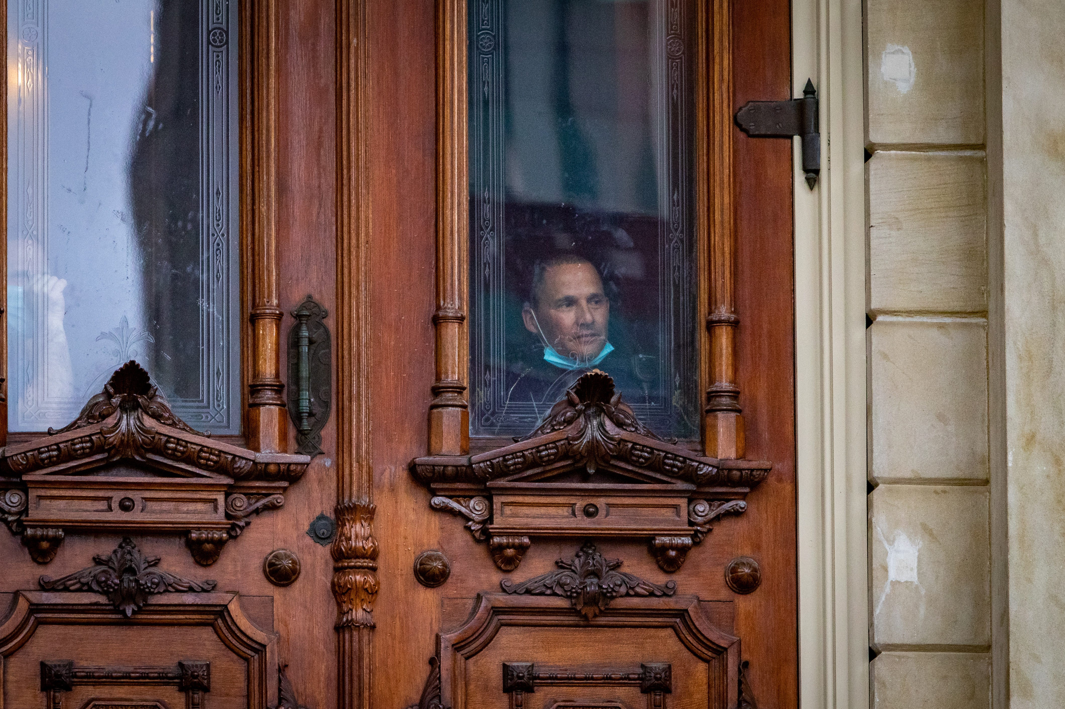 A Michigan State Police officer peers out from inside the capital building at protestors outside.