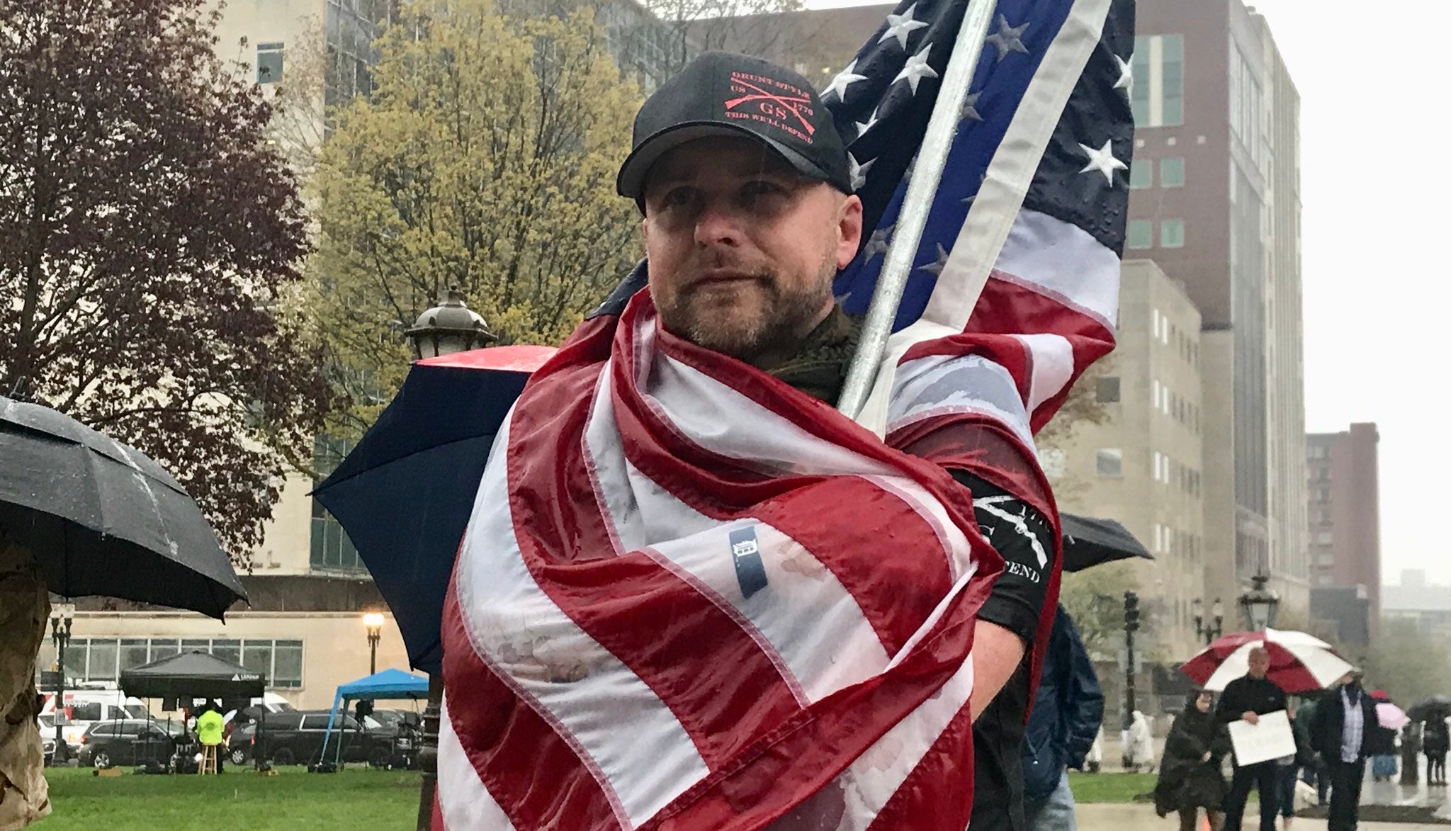 Anthony Jukuri, 36, covers himself with an American flag and watches the protest in the rain.