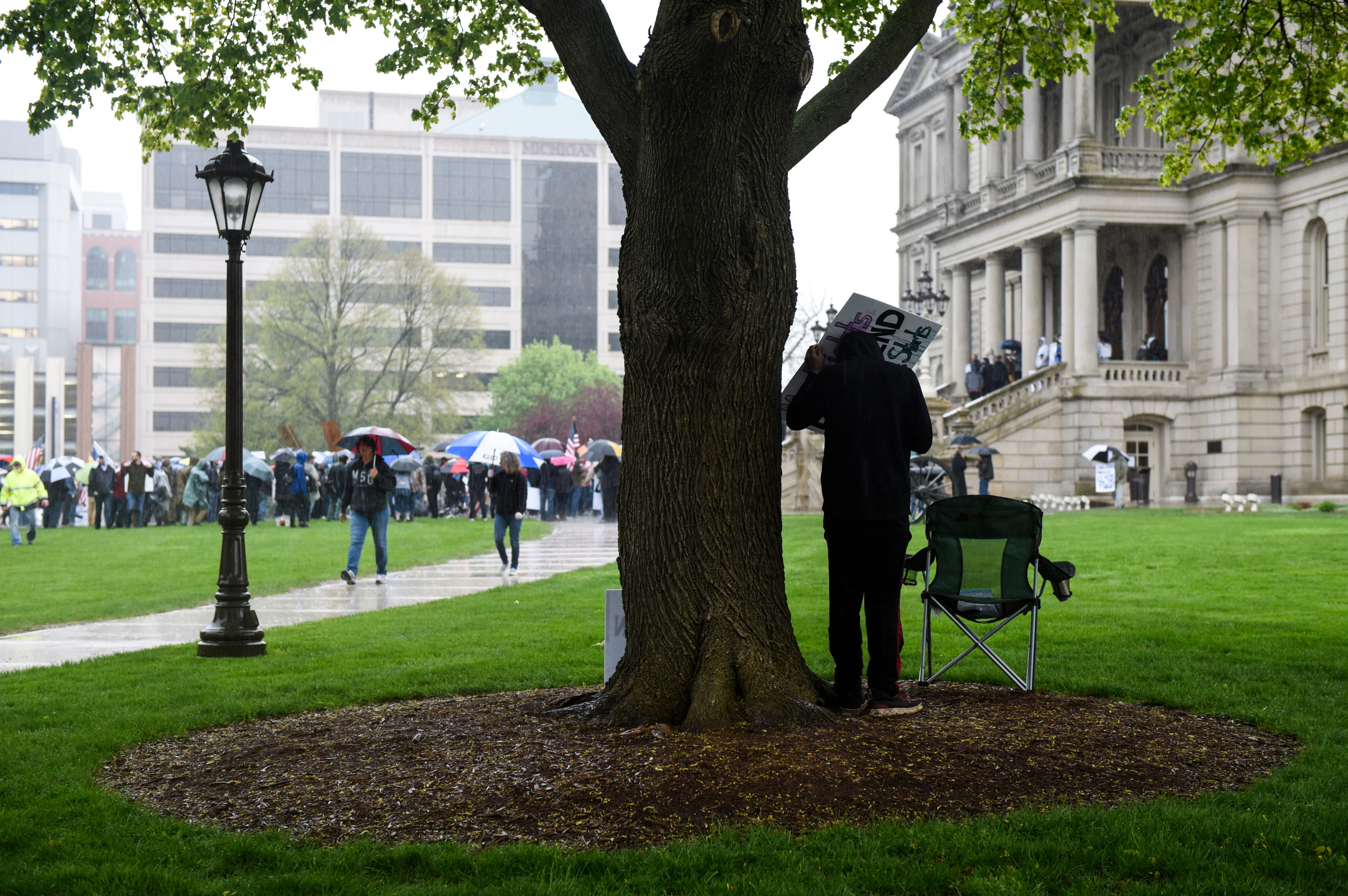 A protester takes shelter from heavy rain under a tree during a protest at the state Capitol.