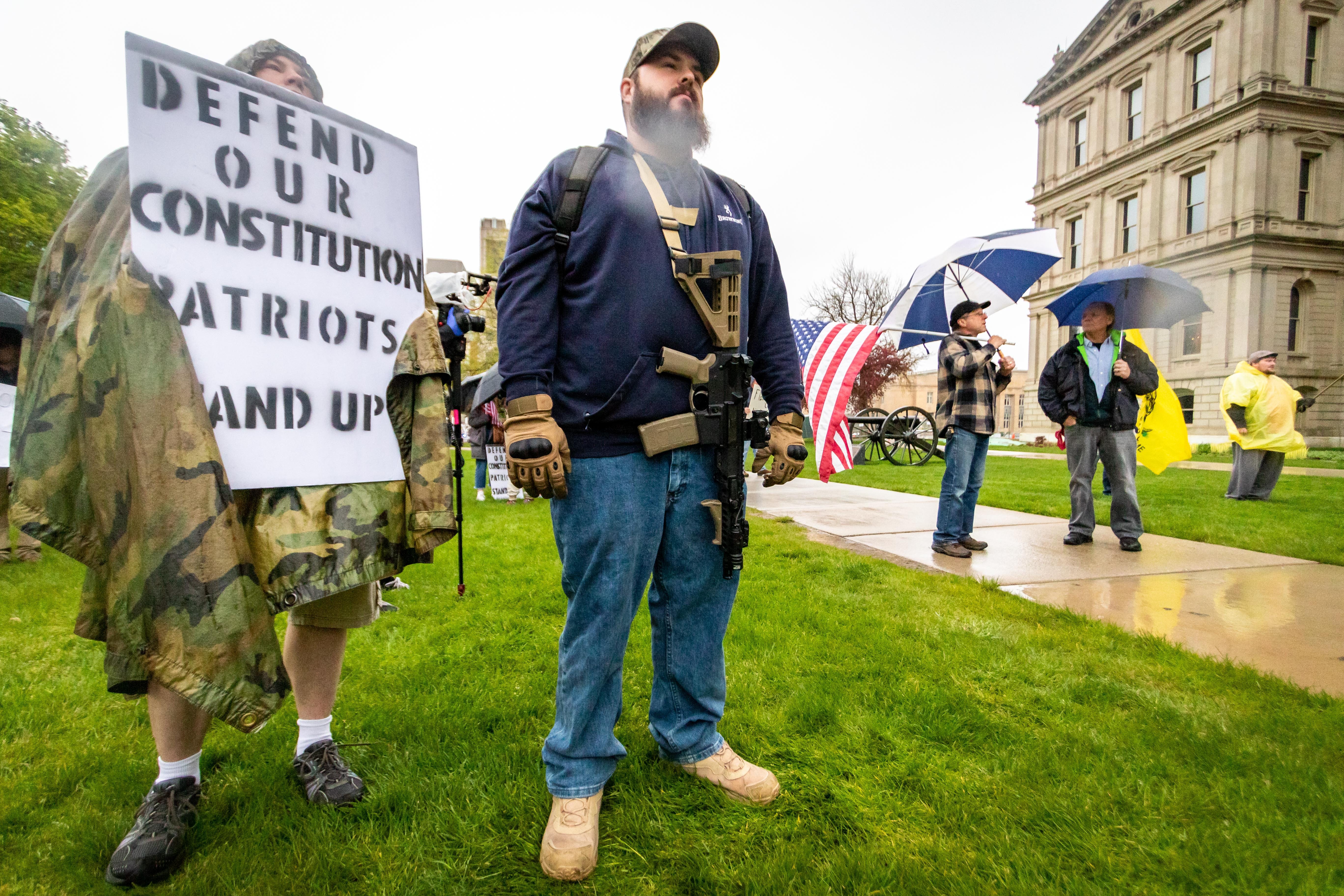Mike Spohn of Detroit stands on the capital lawn with an large gun strapped to his body during the protest