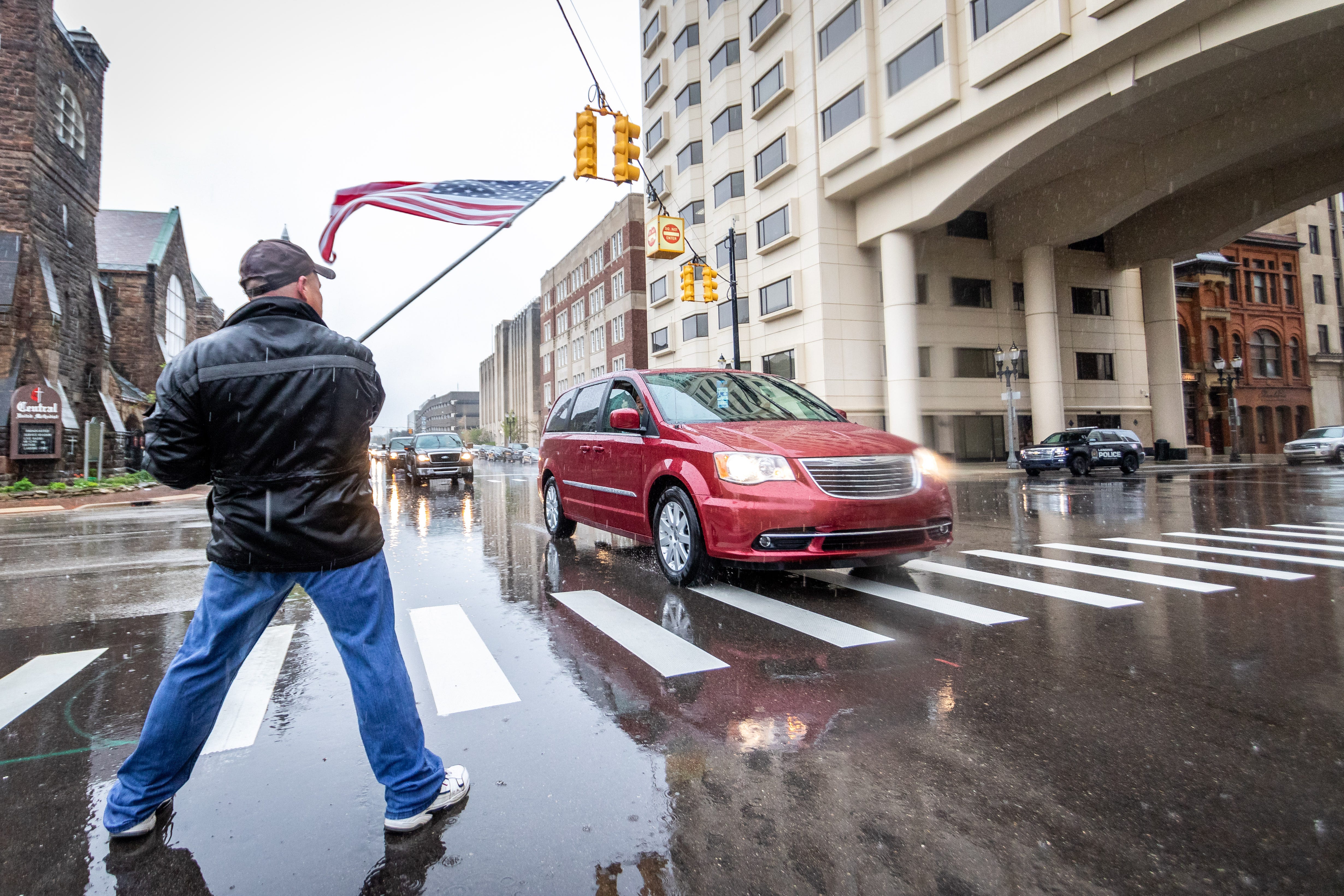 Clay Coey of Lansing waves a flag on the street in front of the Capitol as cars pass by and honk in support.