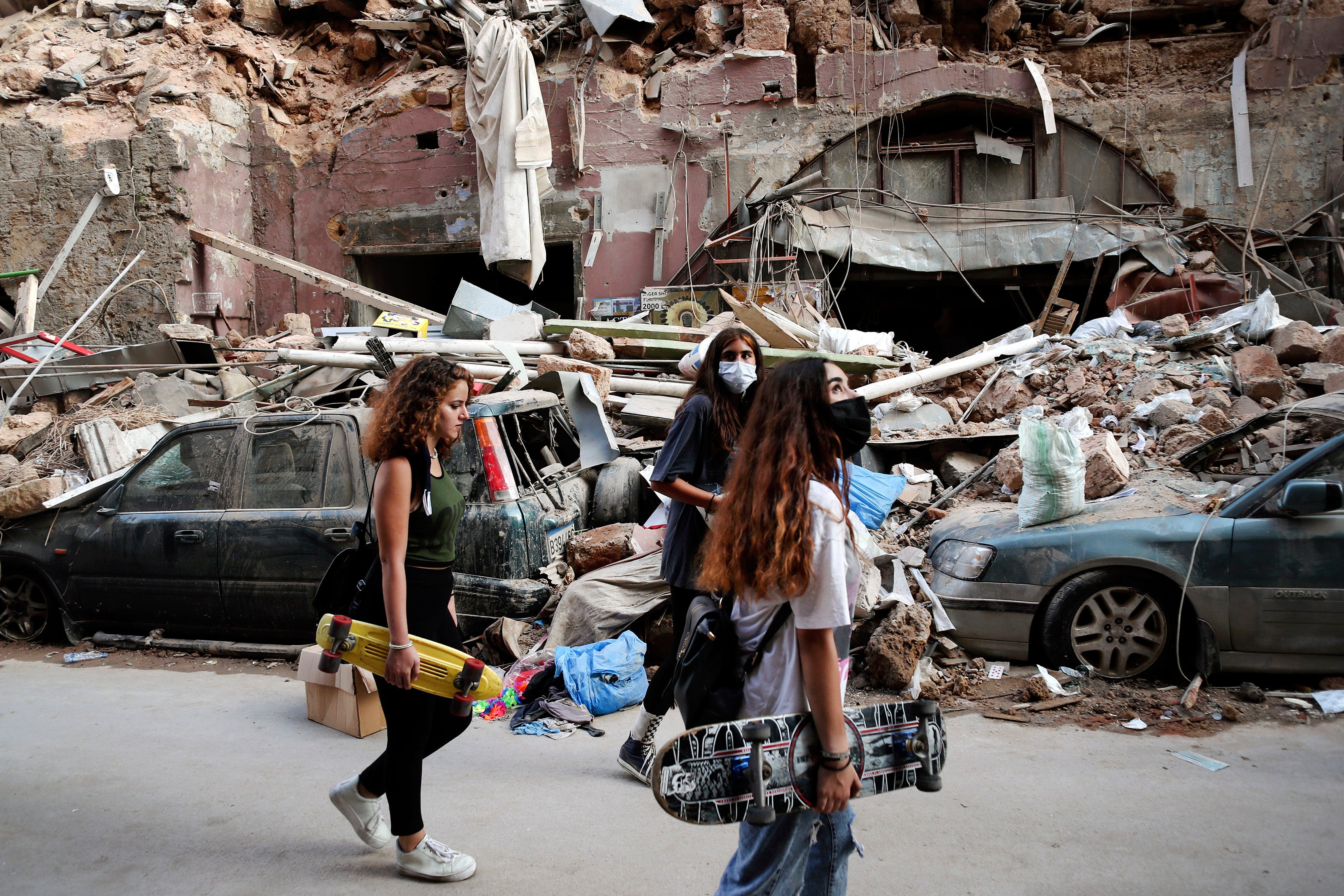 Women walk past destroyed cars at a neighborhood near the scene of Tuesday's explosion that hit the seaport of Beirut, Lebanon, Friday, Aug. 7, 2020. Rescue teams were still searching the rubble of Beirut's port for bodies on Friday, nearly three days after a massive explosion sent a wave of destruction through Lebanon's capital.