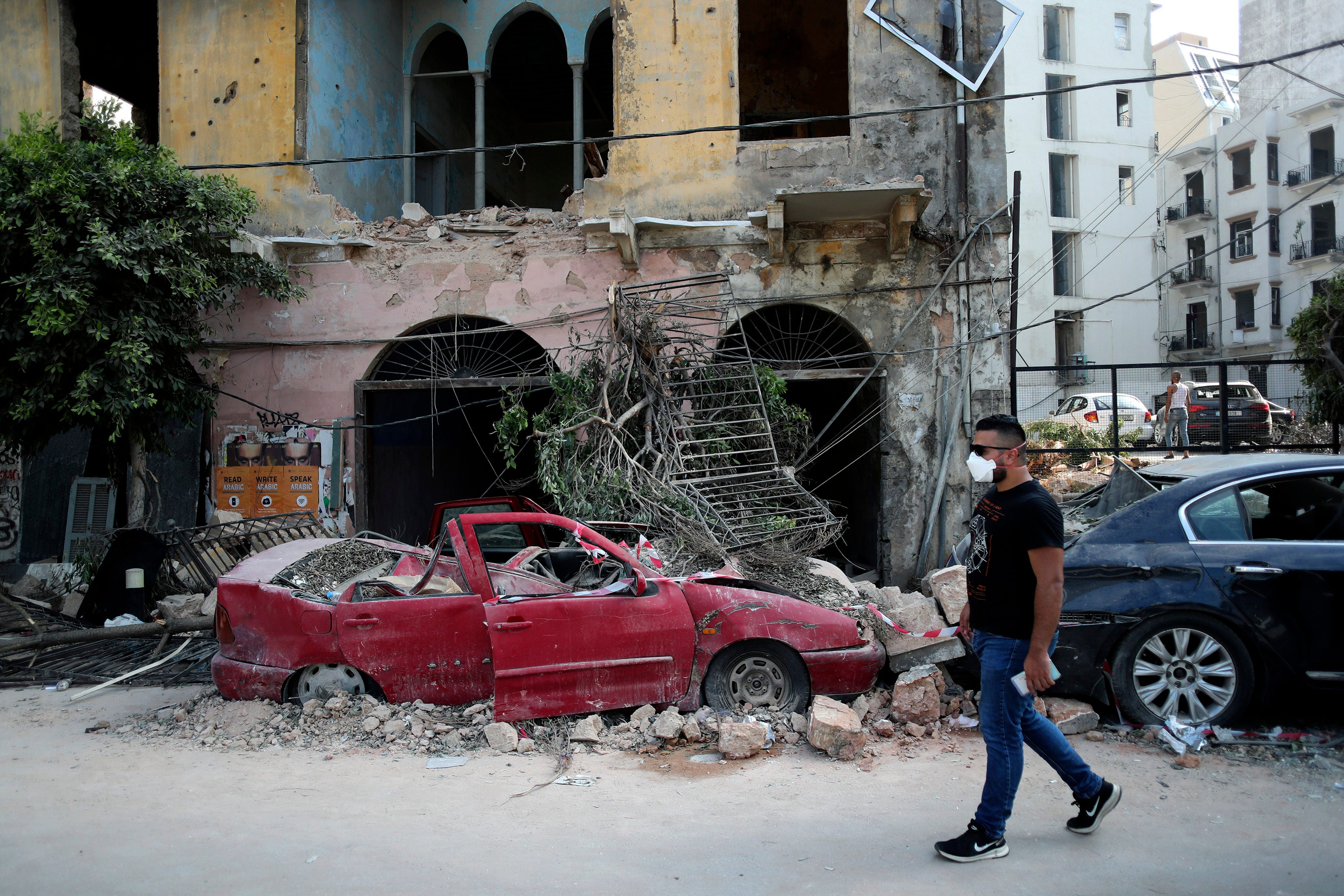 A man walks past a destroyed car at a neighborhood near the scene of Tuesday's explosion that hit the seaport of Beirut, Lebanon, Friday, Aug. 7, 2020. Rescue teams were still searching the rubble of Beirut's port for bodies on Friday, nearly three days after a massive explosion sent a wave of destruction through Lebanon's capital.