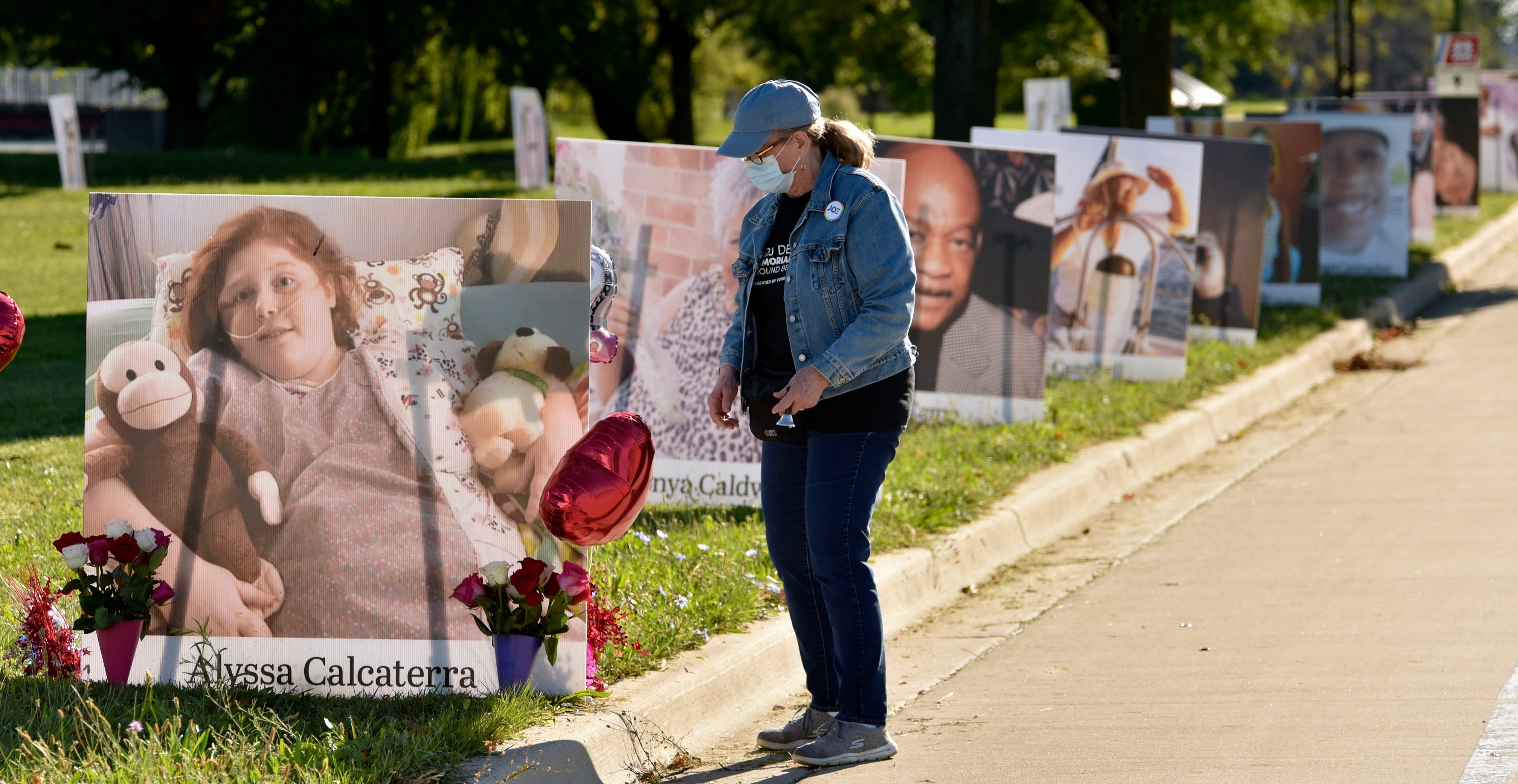 Volunteer Margaret Gore of St. Clair Shores straightens balloons attached to the portrait of COVID-19 victim Alyssa Calcaterra of Madison Heights along The Strand.