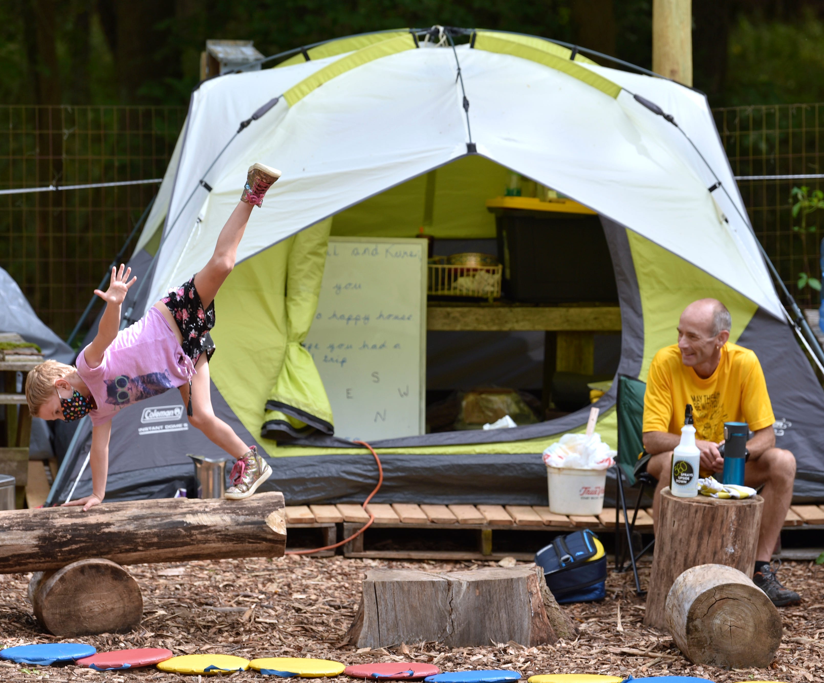 Marley Baldiga, of Oakland, balances on a log as her teacher Robert Crowe, of Lake Orion, watches in front of his tent, the largest in his tent-encampment classroom.