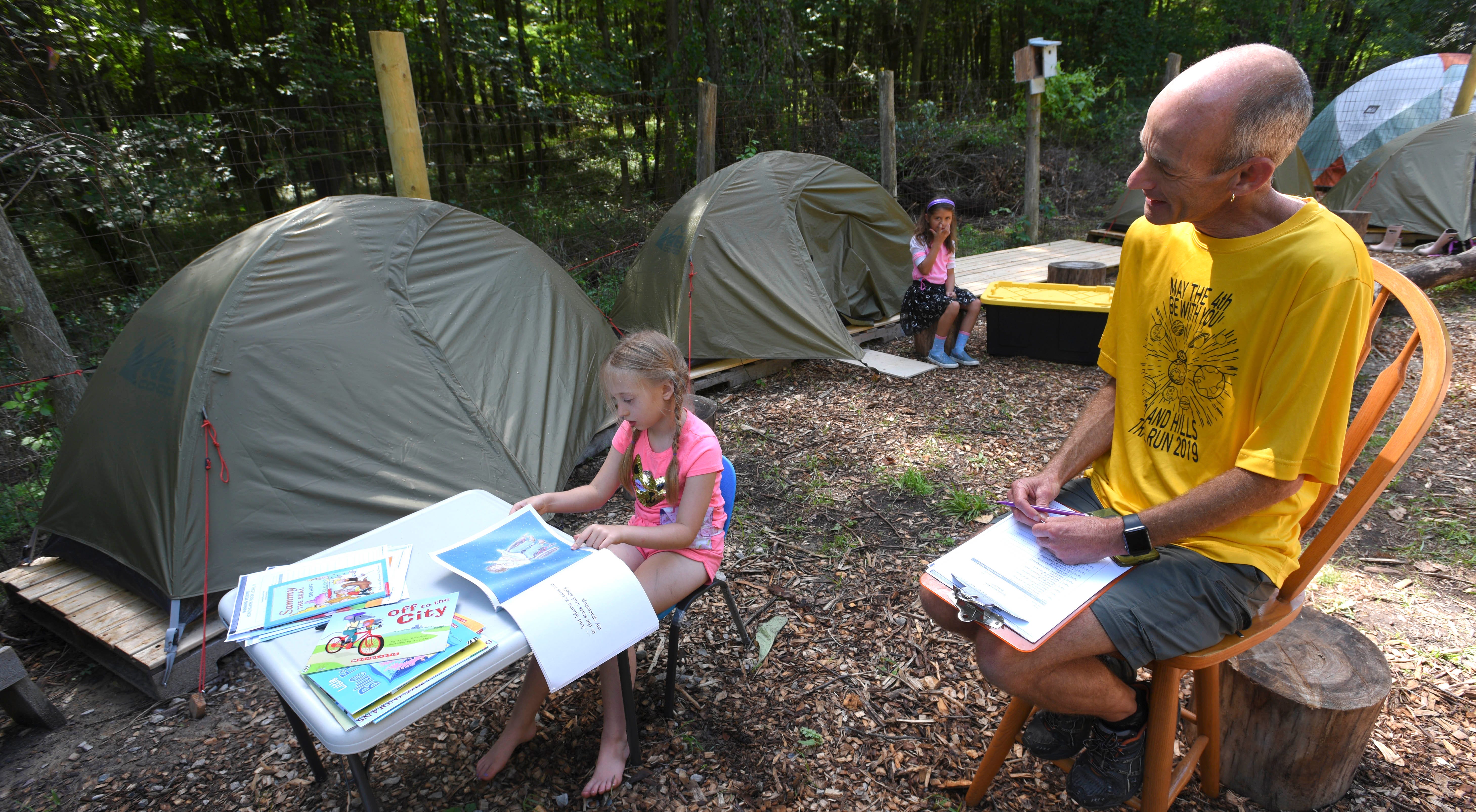 Samantha Young, 7, of Rochester, reads a book as teacher Robert Crowe, of Lake Orion, assesses her reading skills among his classroom, which is a tent encampment.