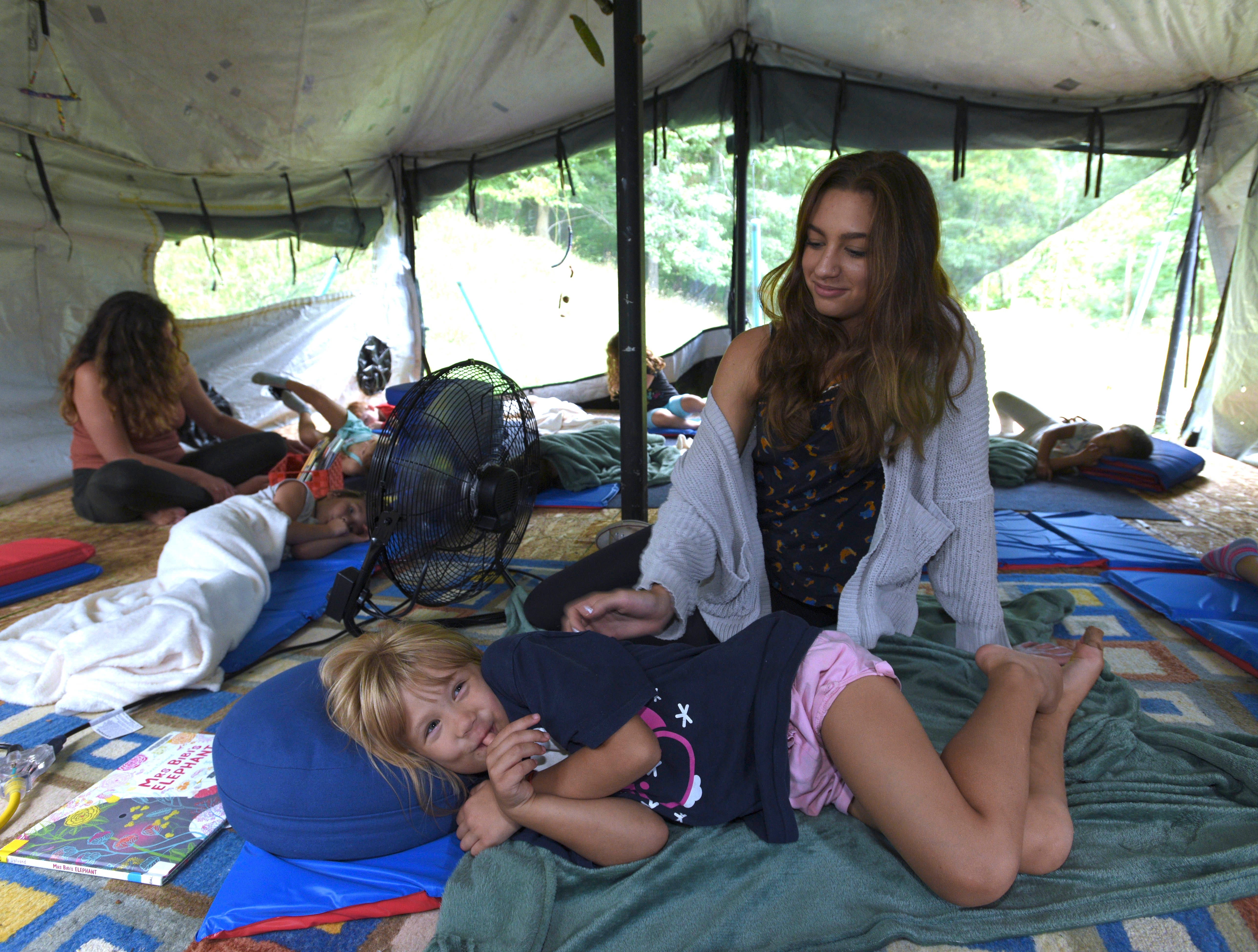 Teacher's aid Olivia Zeiman, right, of Clarkston, rubs the back of six-year-older Daphne Harvat, of Rochester, during nap time in the tent of teacher Melissa Gervais, left, of Oxford.