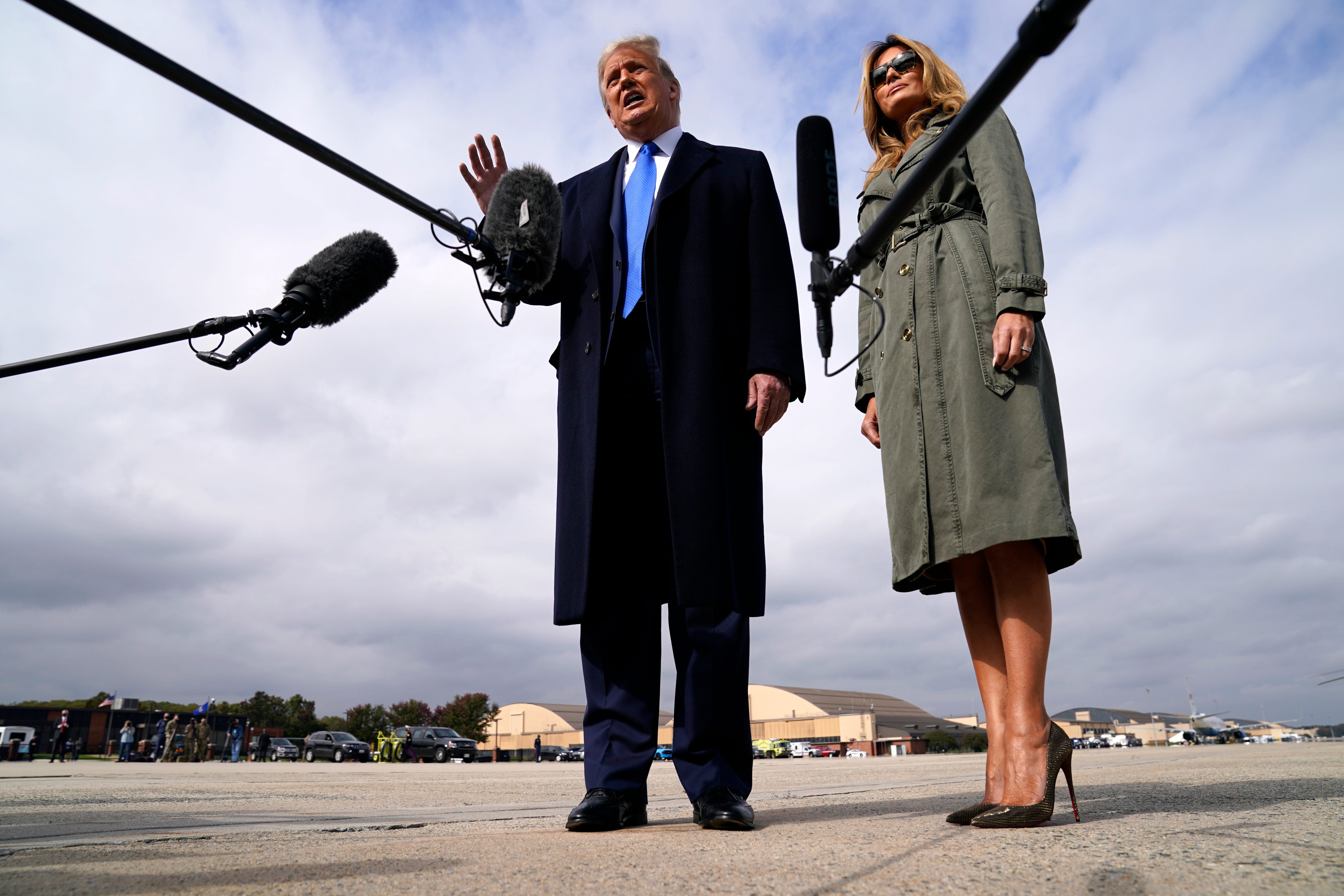 President Donald Trump talks to reporters as first lady Melania Trump listens before boarding Air Force One for a day of campaign rallies in Michigan, Wisconsin, and Nebraska, Tuesday, Oct. 27, 2020, at Andrews Air Force Base, Md. The first lady will be campaigning in Pennsylvania.
