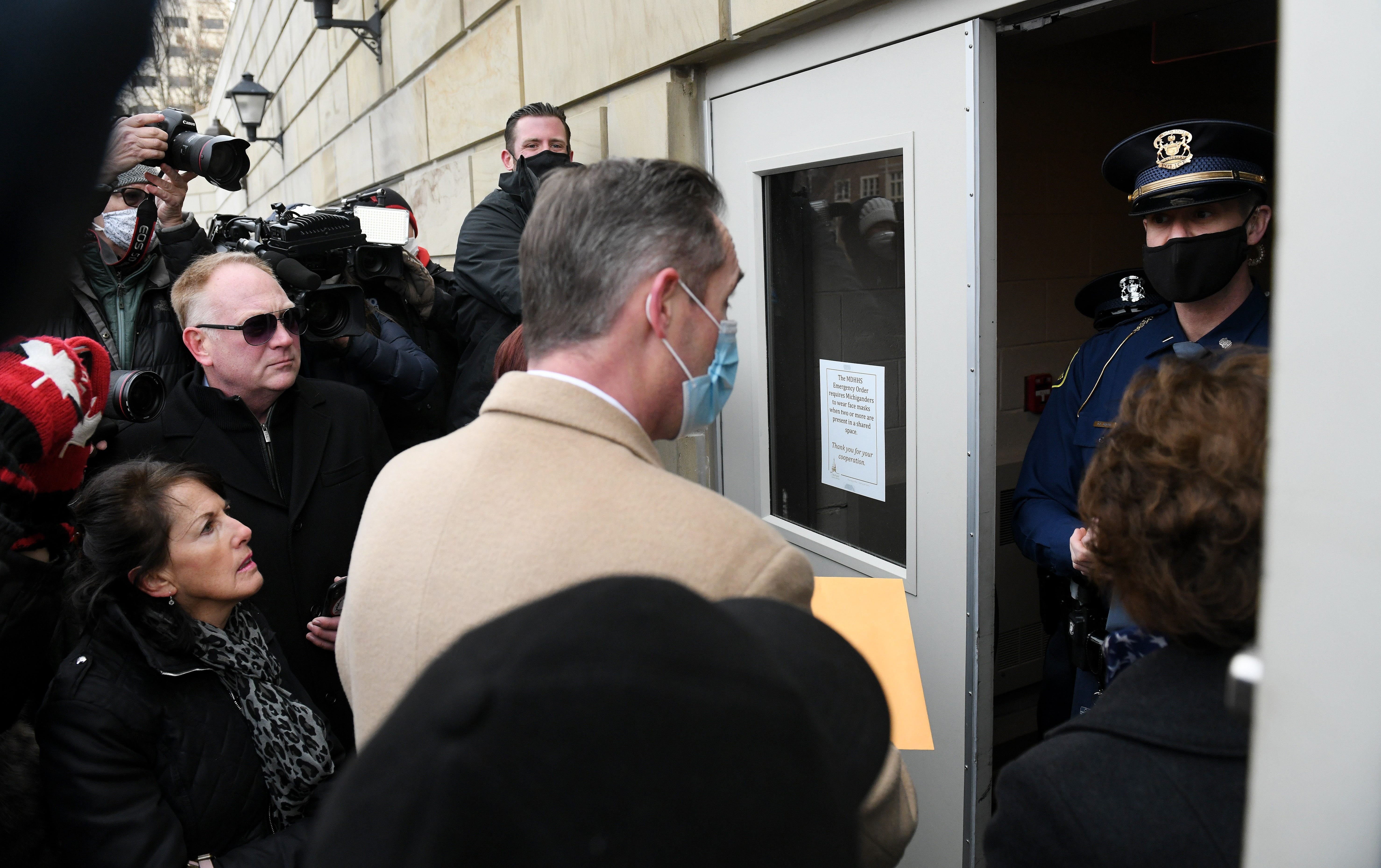 A Michigan State Police officer tells attorney Ian Northon, in tan coat, and Republican electors that they cannot enter the Michigan State Capitol.  At left in sunglasses is state Rep. Matt Maddock.
