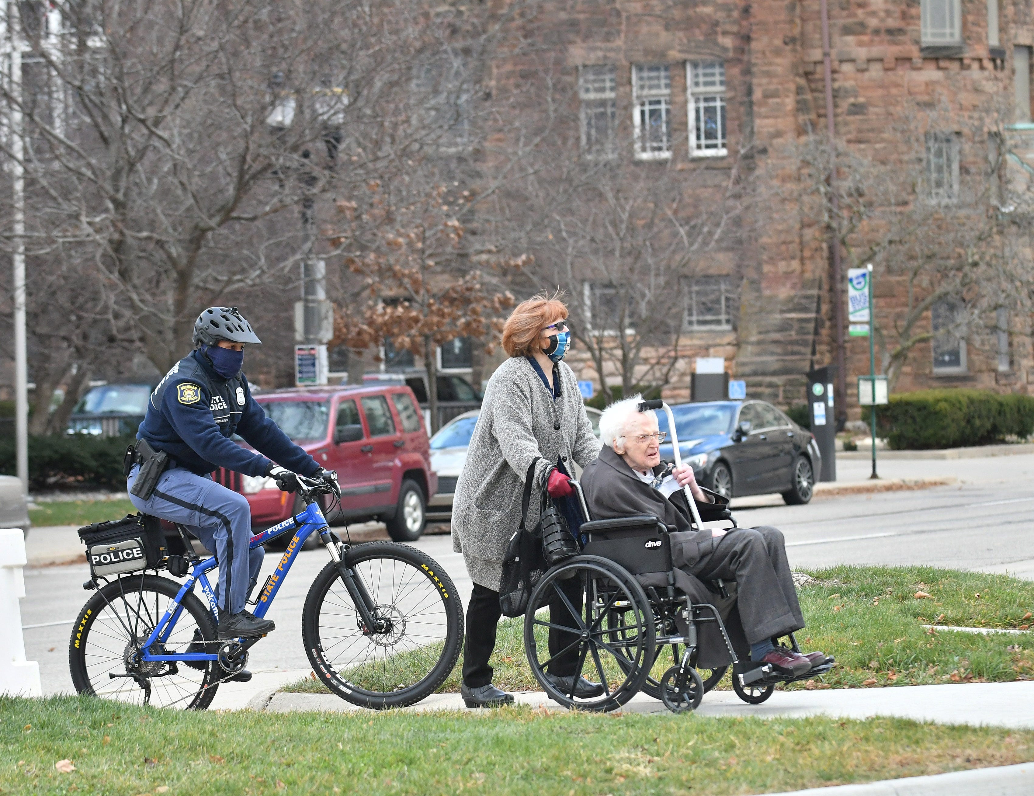 Michigan State Police officers escort Democratic elector Michael Kerwin, 96, with his daughter, Katie Kerwin from the parking garage to the Michigan State Capitol in Lansing, Mich. on Dec. 14, 2020.   The electors are casting their votes today at the capitol for the president and vice president.