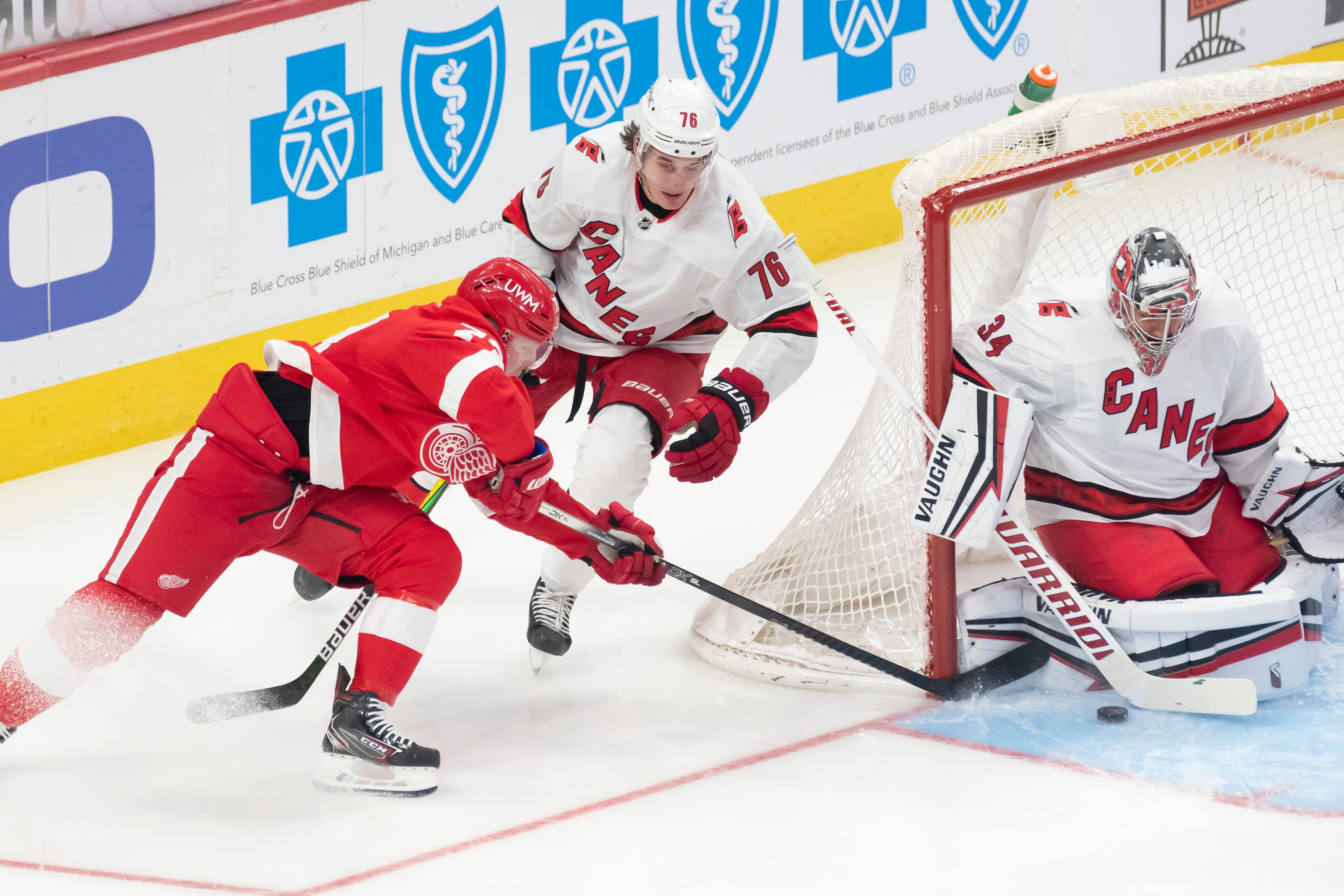Detroit left wing Adam Erne, left, tries to get the puck past Carolina defenseman Brady Skjei and goaltender Petr Mrazek in the first period during a game between the Detroit Red Wings and the Carolina Hurricanes, at Little Caesars Arena, in Detroit, January 14, 2021.
