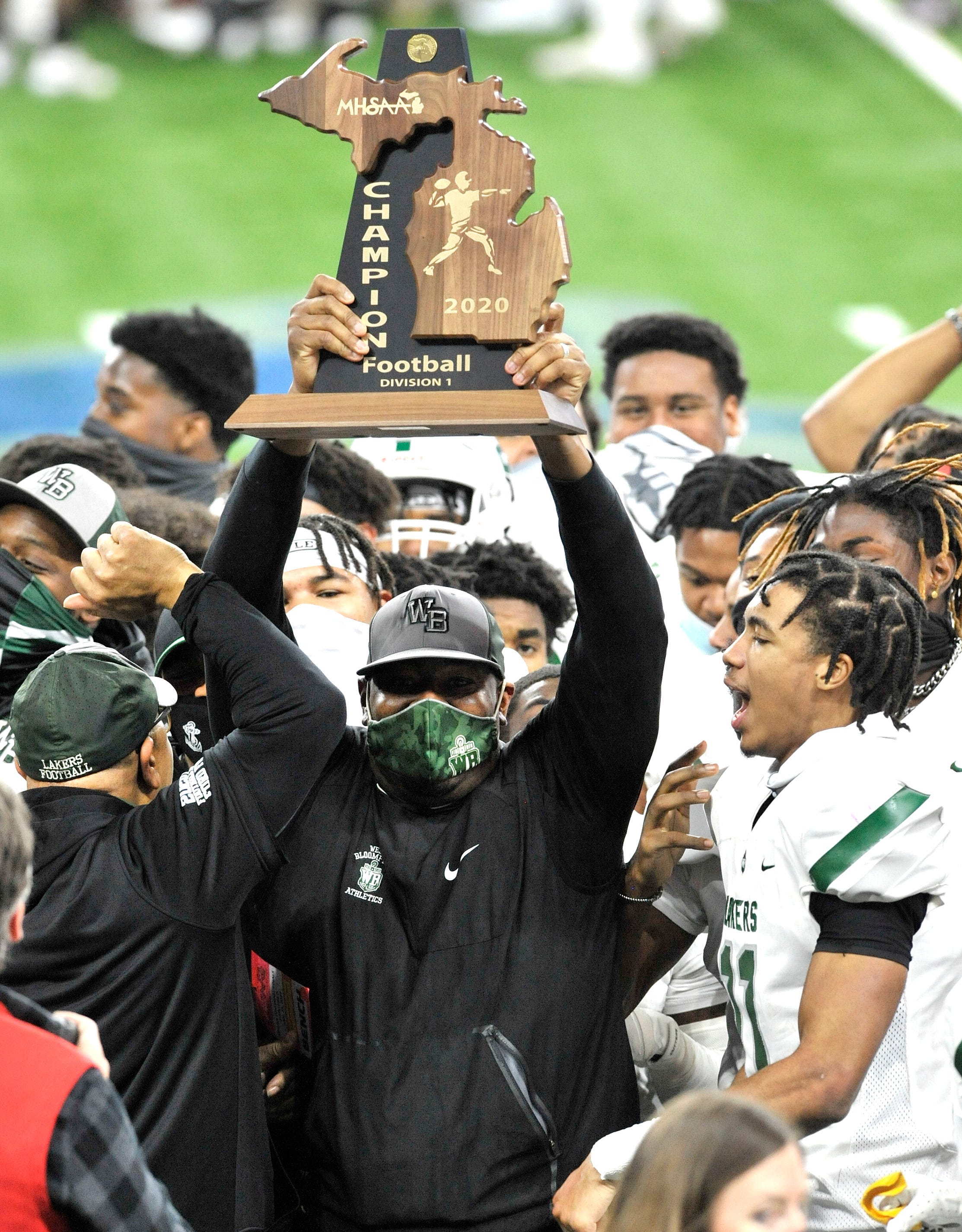 West Bloomfield head coach Ron Bellamy jumps up and down with his team's championship trophy for the MHSAA Division 1 finals at Ford Field against Davison