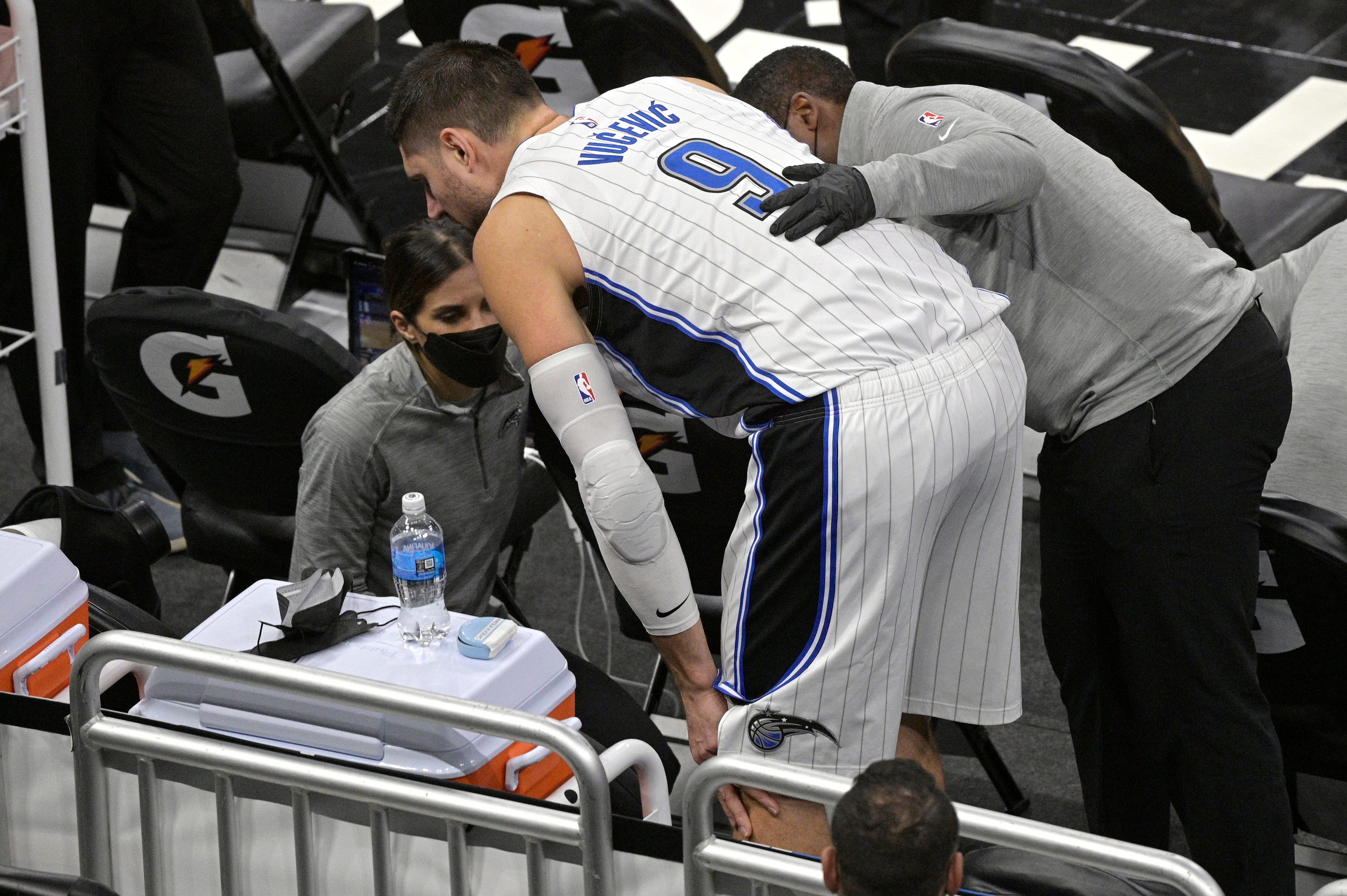 Orlando Magic center Nikola Vucevic (9) holds his knee as he is helped by trainers behind the bench area during the first half of an NBA basketball game against the Detroit Pistons.