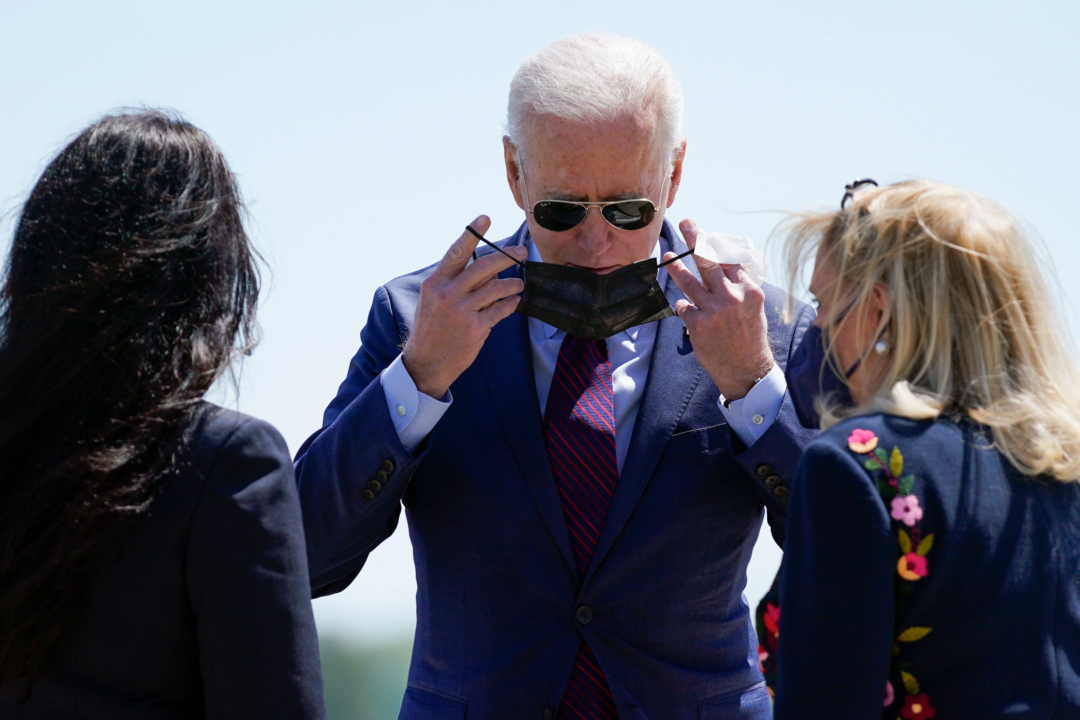 President Joe Biden puts on his face mask as he is greeted by Rep. Rashida Tlaib, D-Mich., left, and Rep. Debbie Dingell, D-Mich, as he arrives at Detroit Metropolitan Wayne County Airport.
