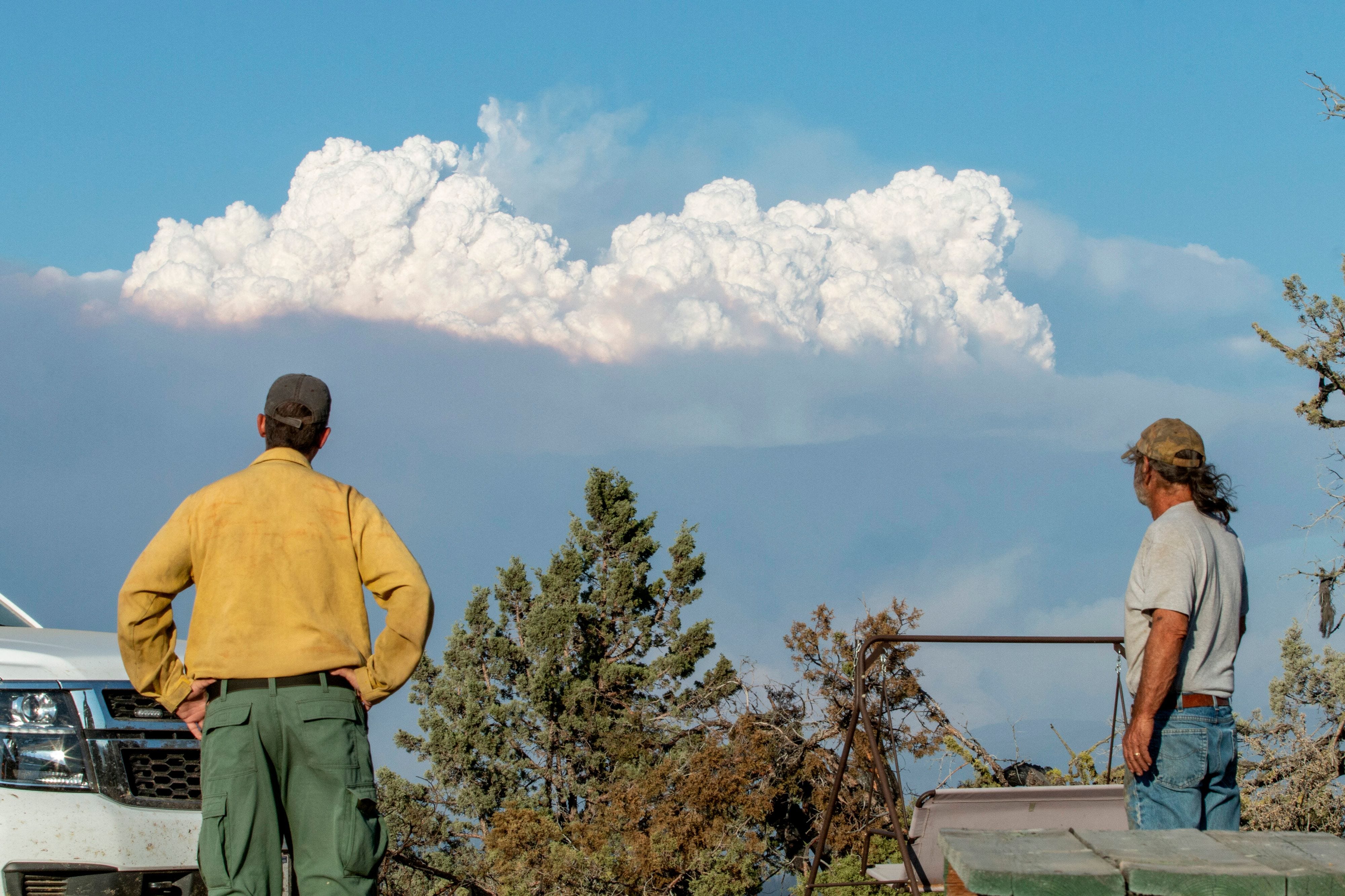 Fire Mitigation and Education Specialist Ryan Berlin (L) and  home owner Bob Dillon watch the Bootleg Fire smoke cloud from Dillon's home in Beatty, Oregon, on July 16, 2021. - The extreme drought-hit western United States braced for more wildfire destruction July 16, 2021 as efforts to contain a vast blaze scorching southern Oregon failed to progress, and dangerous dry lightning storms were forecast in California. The Bootleg Fire near Oregon's border with California grew overnight to 240,000 acres -- larger than New York City, and by far the biggest active blaze in the US -- while remaining just seven percent contained.