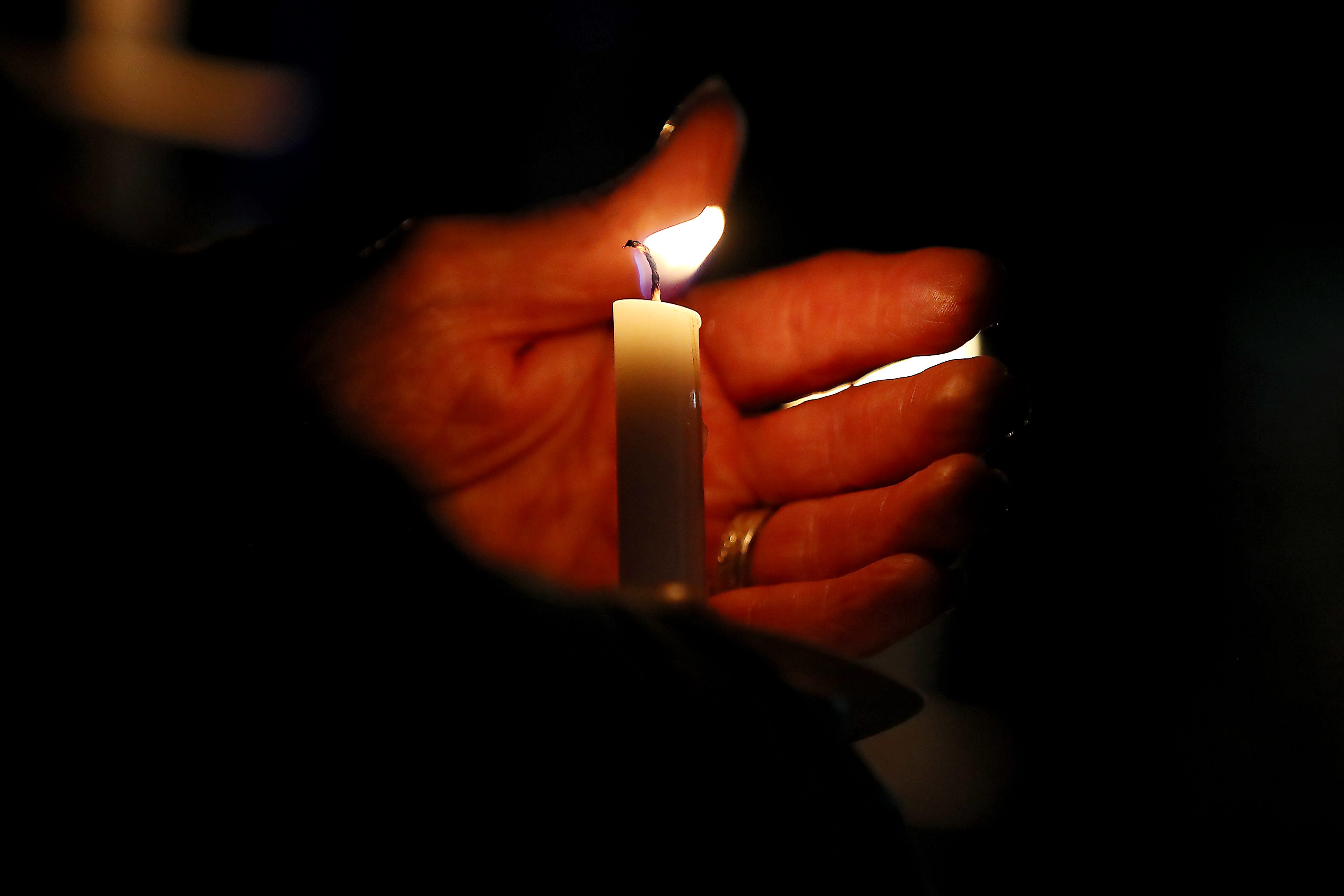 A person tries to block the wind from blowing out their candle during a candlelight vigil in downtown Oxford on Friday, Dec. 3, 2021.
