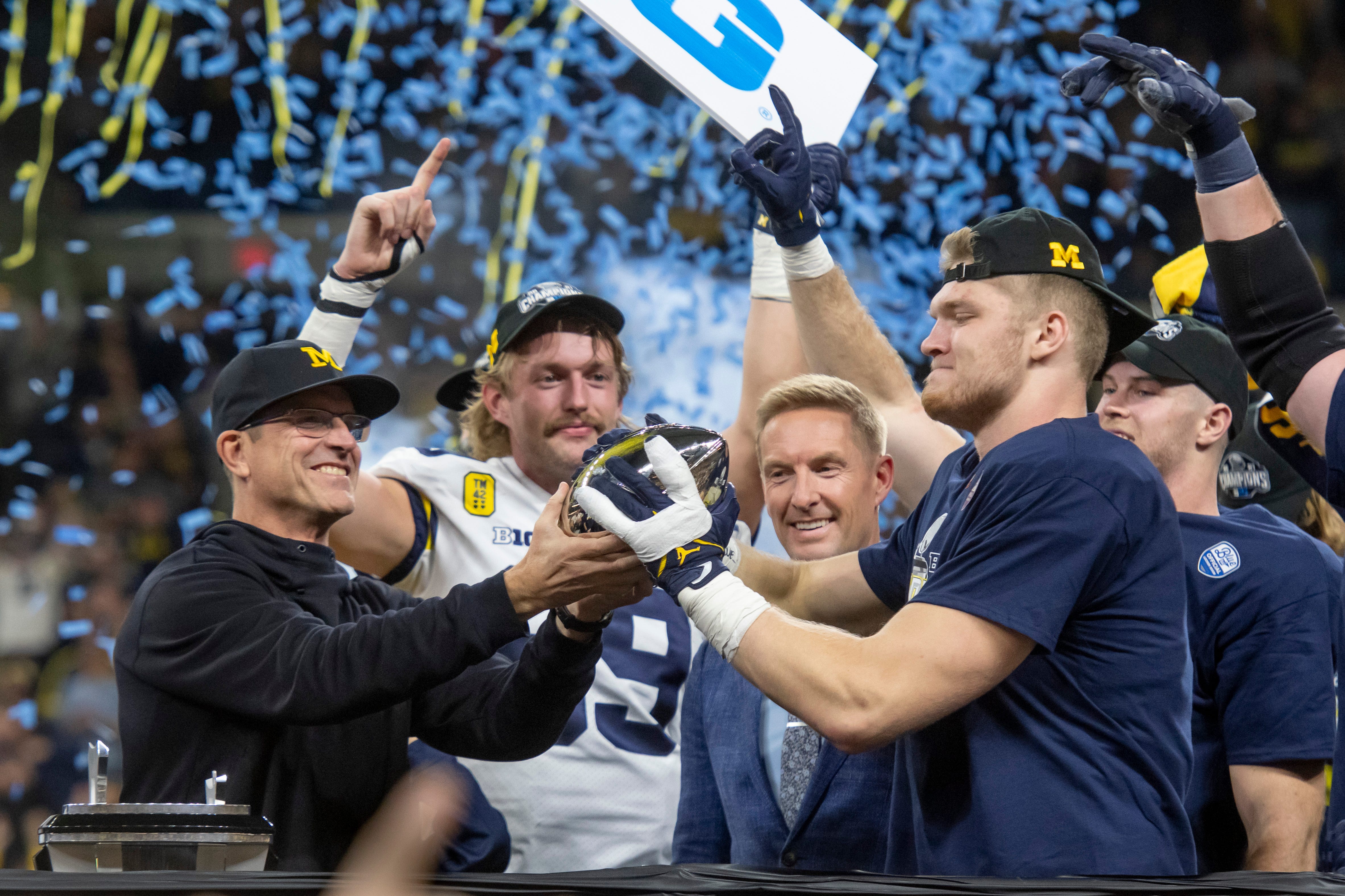 Head coach Jim Harbaugh hands the championship trophy to defensive end Aidan Hutchinson after the University of Michigan defeated the University of Iowa 42-3 to win the Big Ten championship at Lucas Oil Stadium in Indianapolis, December 5, 2021.