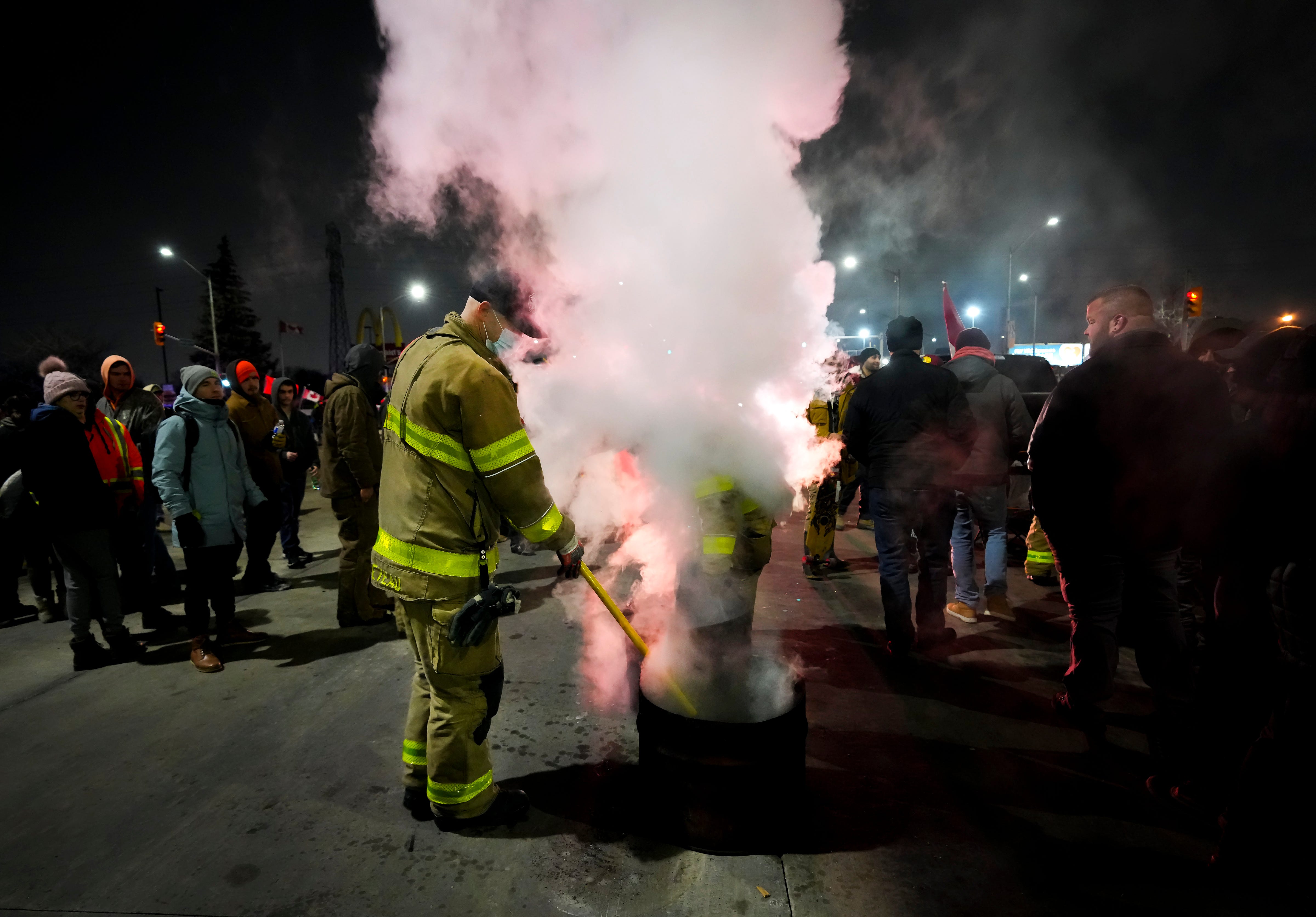 Firefighters put out a burning barrel fire as truckers and supporters block the access leading from the Ambassador Bridge, linking Detroit and Windsor, as truckers and their supporters continue to protest against the COVID-19 vaccine mandates and restrictions in Windsor, Ontario, on Wednesday, Feb. 9, 2022.