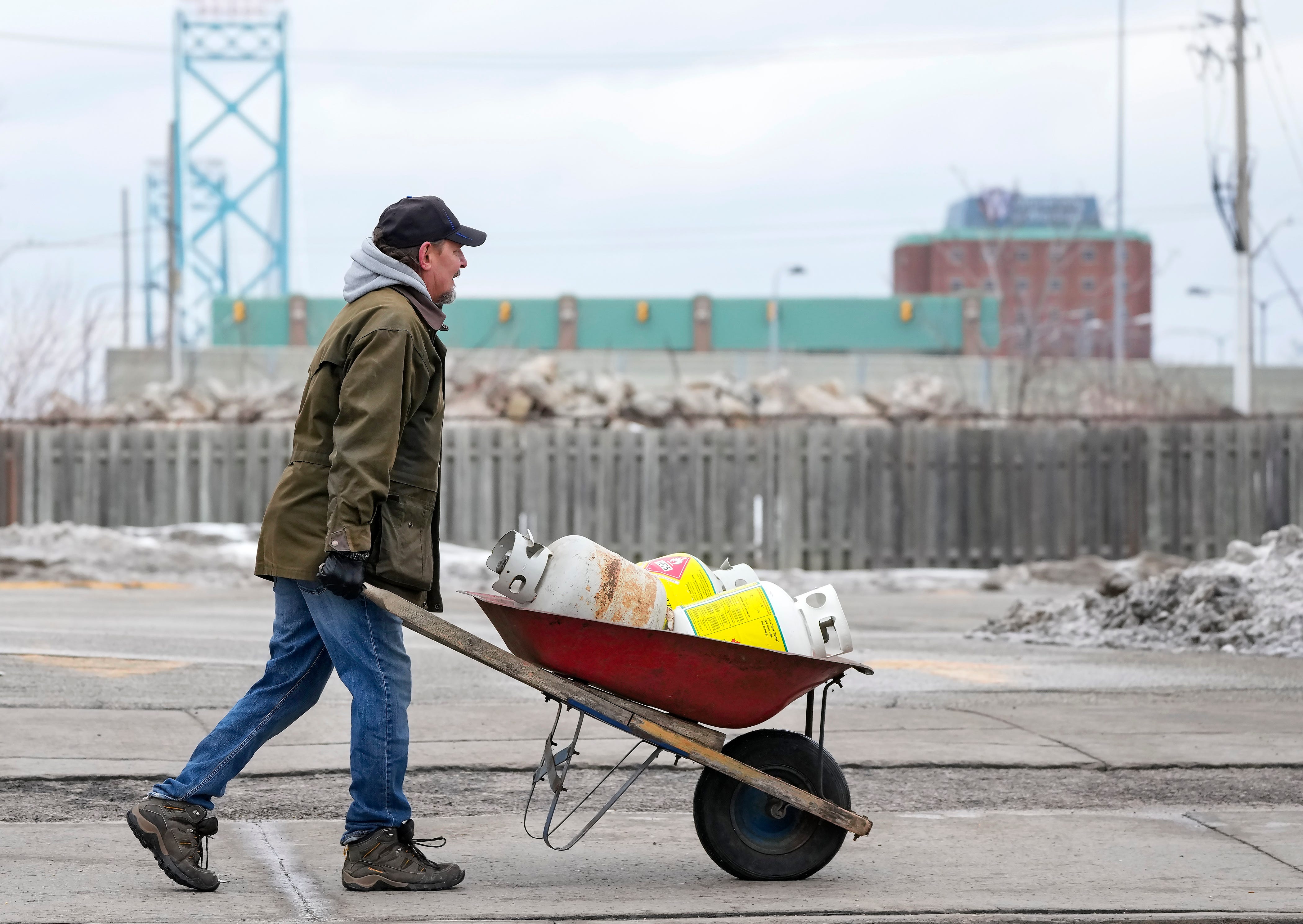 Truckers and supporters carry propane tanks past police to where they are blocking the access leading from the Ambassador Bridge, linking Detroit and Windsor, as truckers and their supporters continue to protest against the COVID-19 vaccine mandates and restrictions, in Windsor, Ontario, Thursday, Feb. 10, 2022.