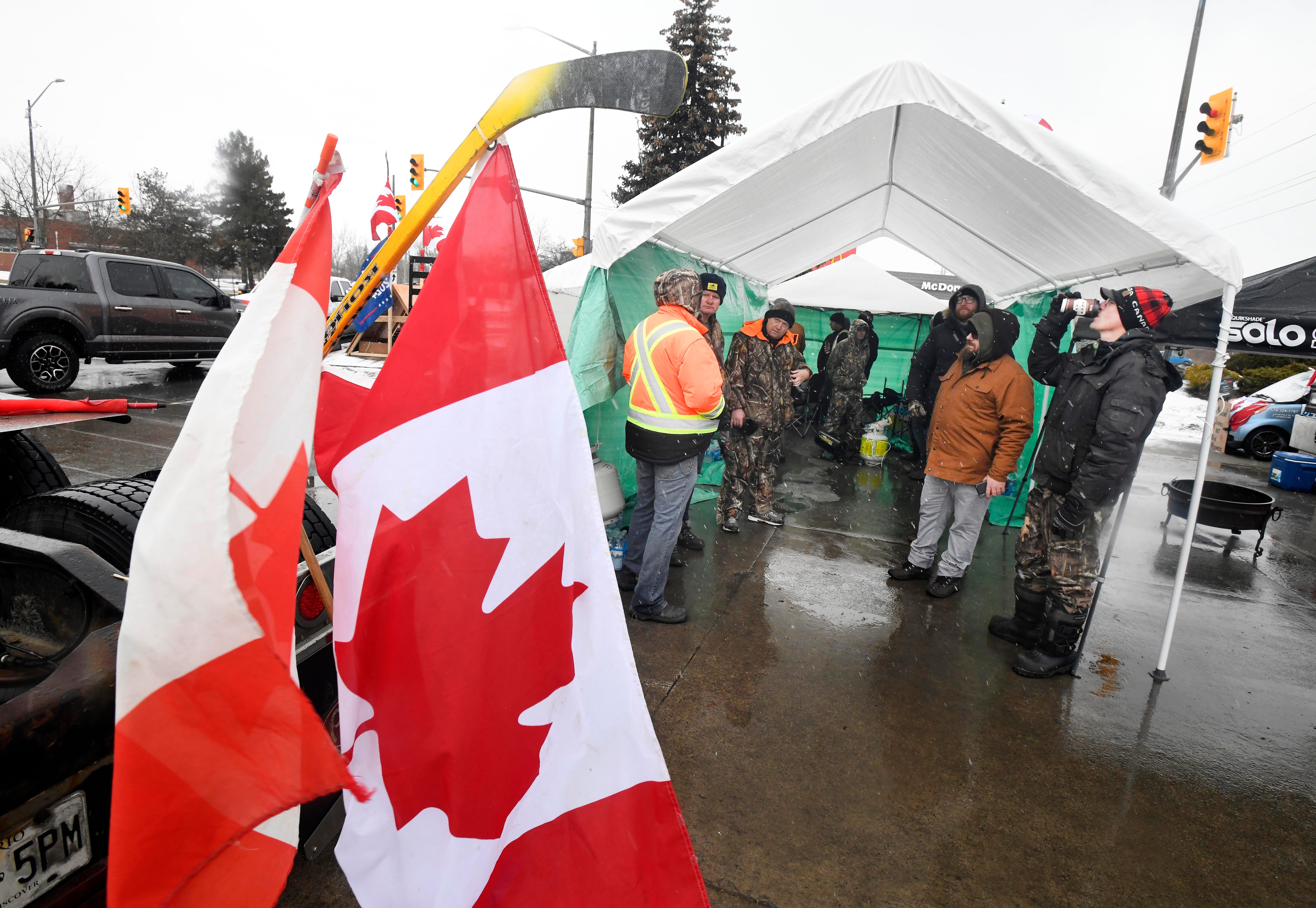 Protestors take shelter from the cold weather with Canadian flags on hockey sticks throughout the camp.  Canadian truckers protests against COVID measures on corner of Huron Church Road and Tecumseh, with the Ambassador Bridge in the background, in Windsor, Canada on February 11, 2022.