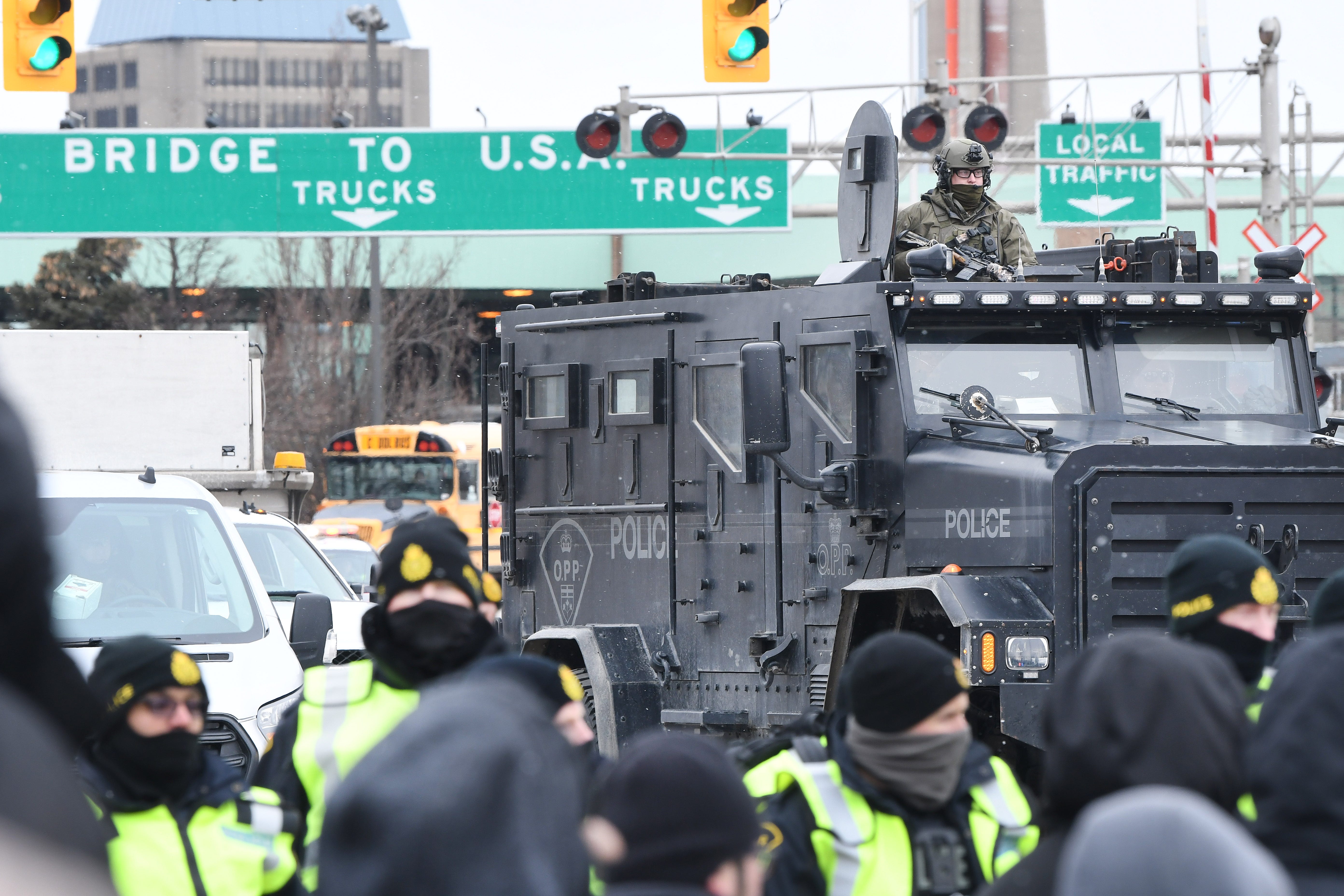 An armored vehicle slowly follows law enforcement officers as they walk a line through protestors unhappy over Canada ' s COVID mandates, near the Ambassador Bridge in Windsor, Canada, on February 12, 2022.