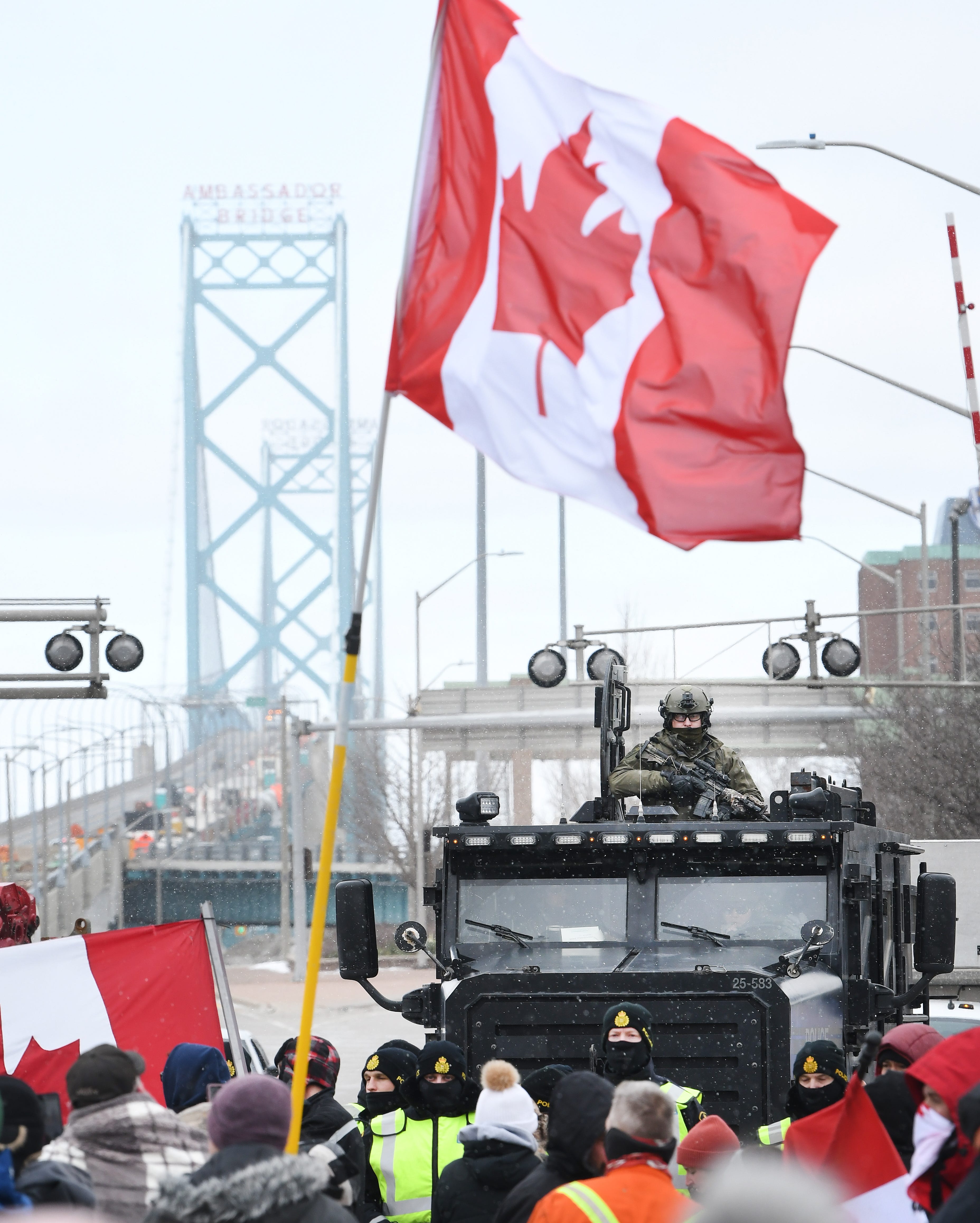 An armored vehicle slowly follows law enforcement officers as they walk a line through protestors unhappy over Canada ' s COVID mandates, near the Ambassador Bridge in Windsor, Canada, on February 12, 2022.