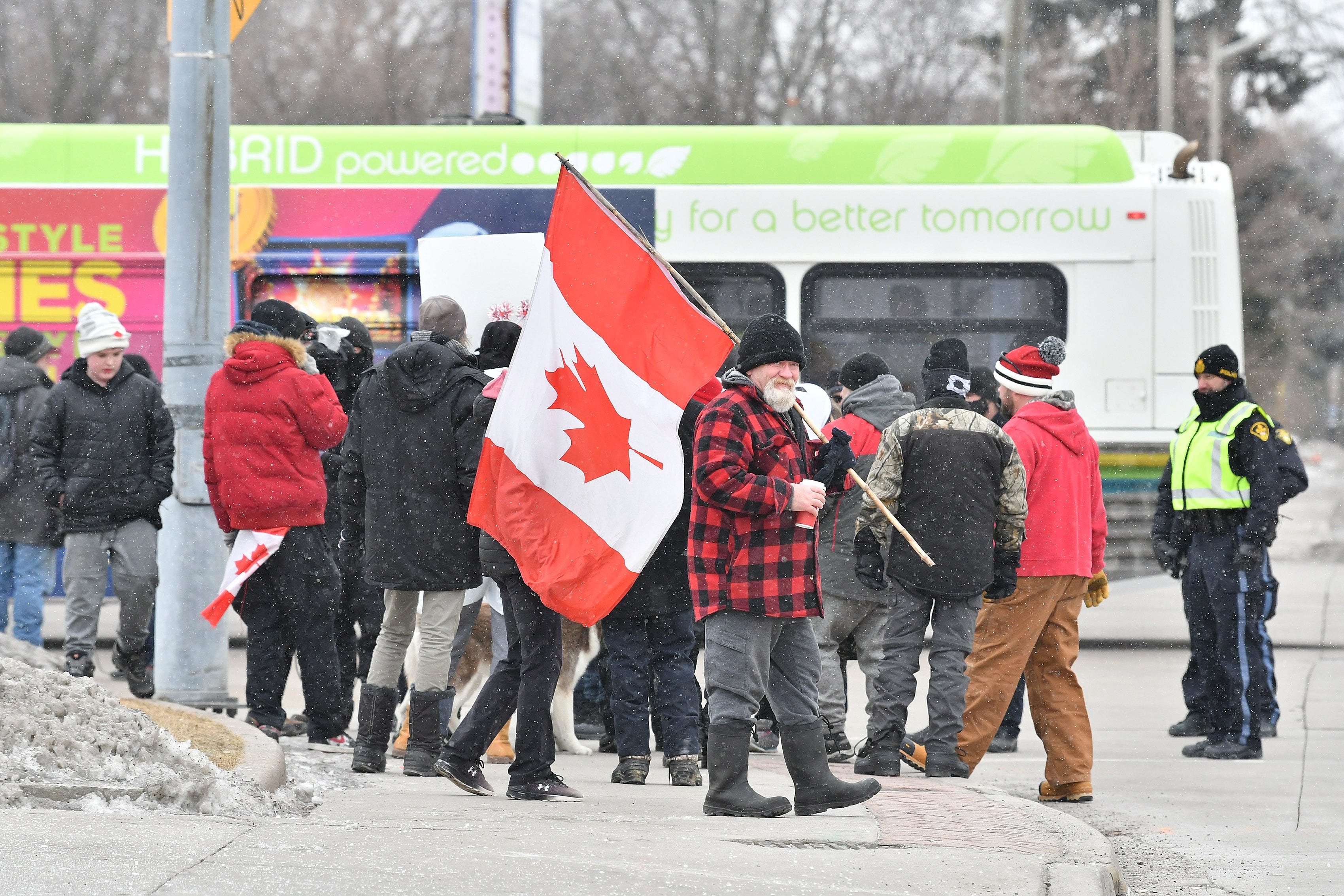 Protesters gather on the sidewalk of Tecumseh Road in view of the combined police presence in Windsor, Ontario, on Feb. 13, 2022.  The city bus in the background was used to transport police officers.
(Robin Buckson / The Detroit News)