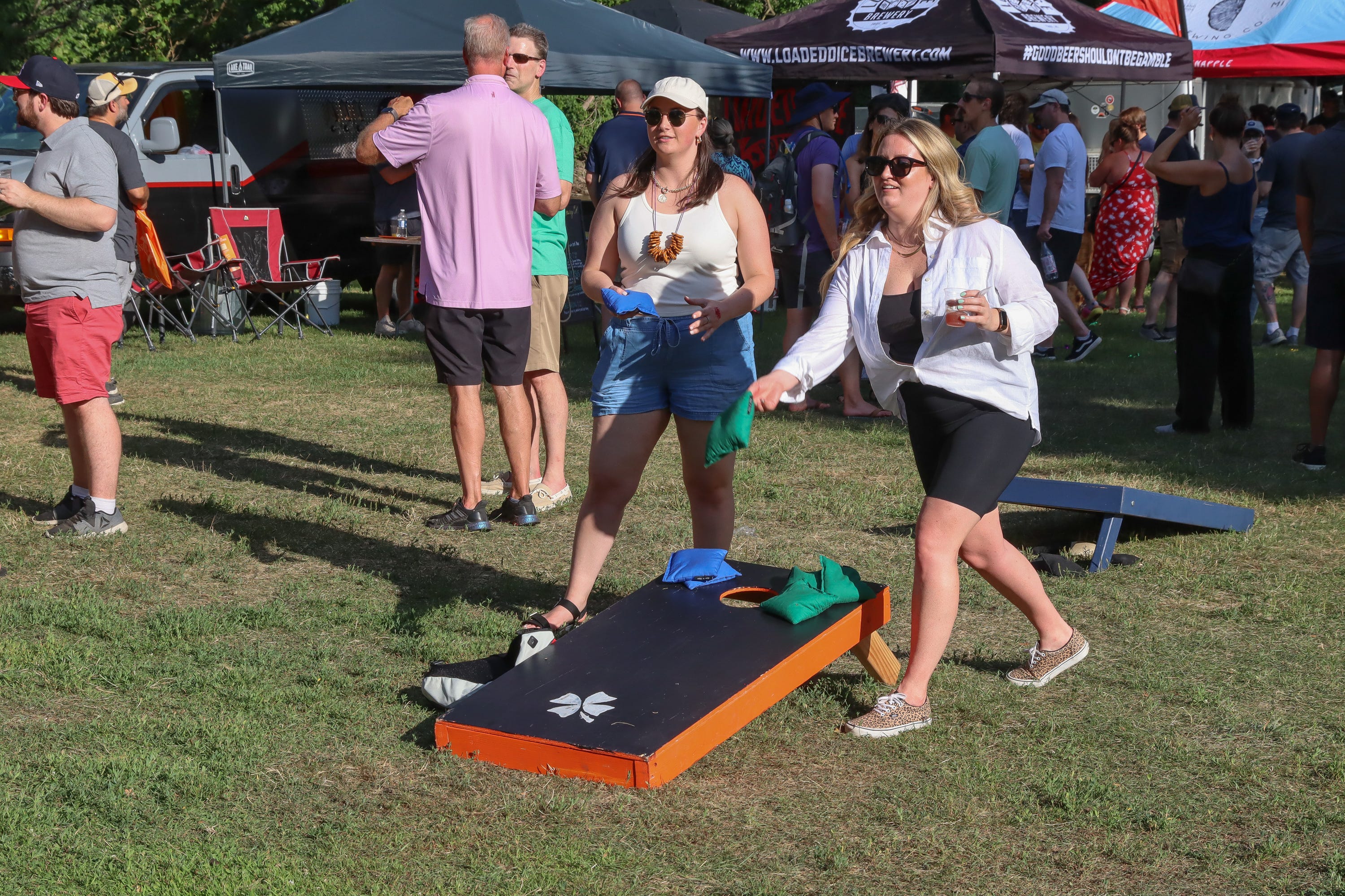 Maddie Davis, of Ann Arbor, looks on as Heather Dangel, of Livonia, tosses a cornhole bag at the New Holland Brewing area at the Michigan Brewers Guild Summer Beer Festival Friday in Ypsilanti's Riverside Park. Dangel doesn't spill a drop.