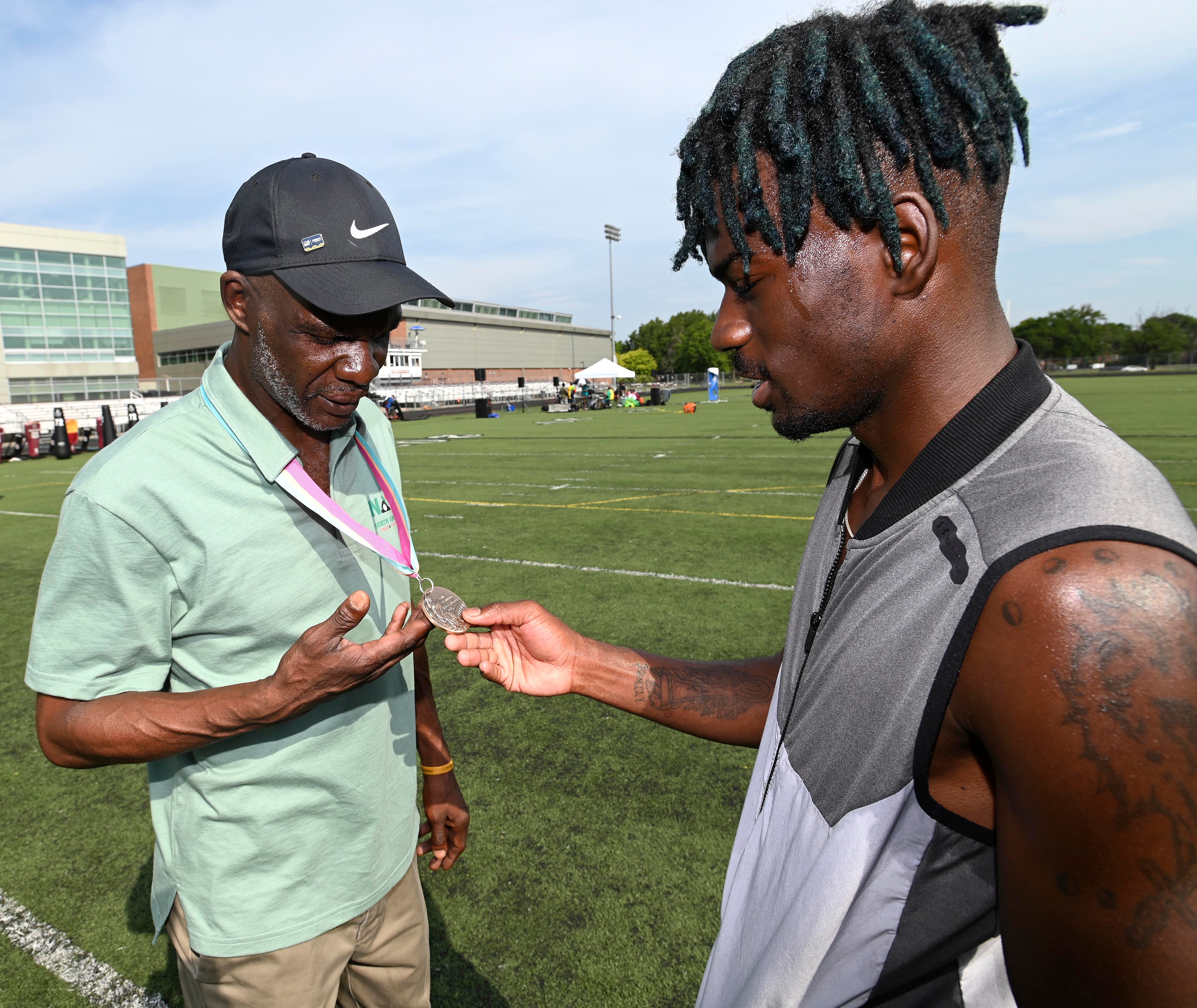 Earl Jones, left, shows his Olympic medal to Montel Lewis, 21, of Detroit, Saturday morning, Aug. 20, 2022. Jones won a bronze medal in the 800-meter run in the 1984 Olympics.