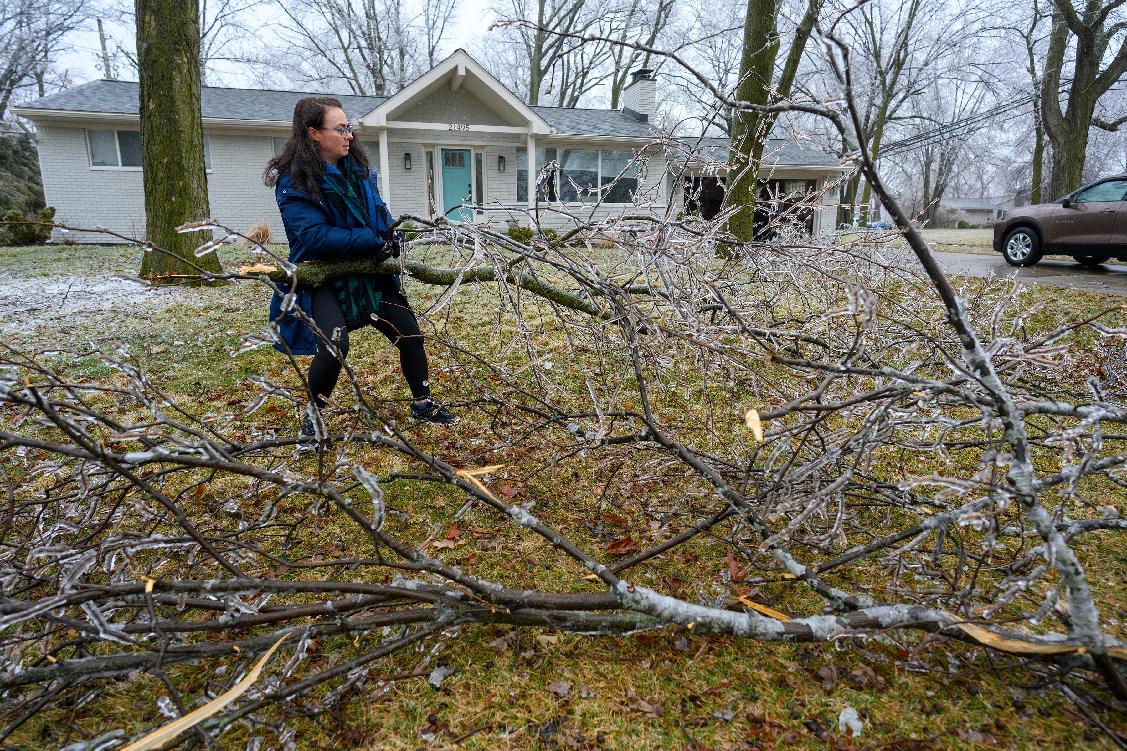 Kathleen Nachtrab moves broken tree branches to the curb after ice brought them down on her property on Grosse Ile, Thursday, February 23, 2023.