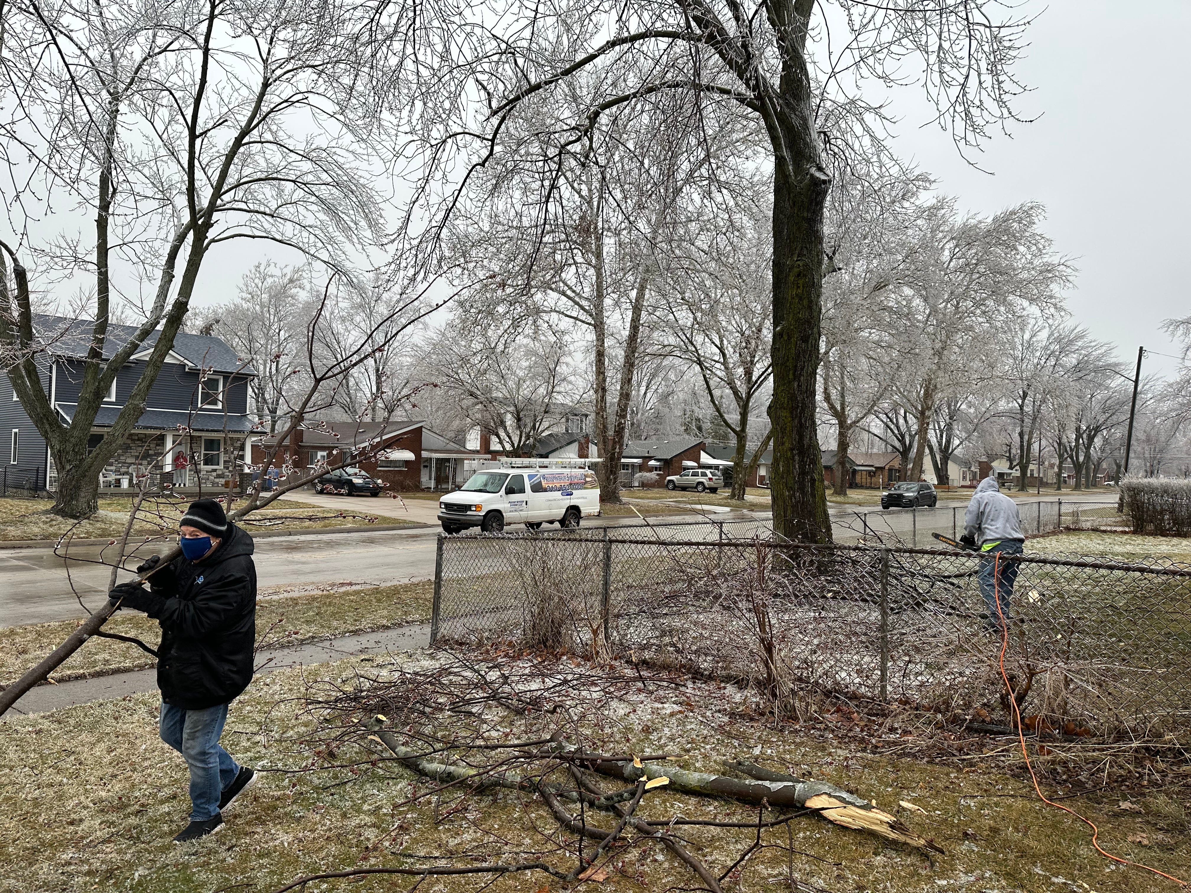 Rich Dennis, 80, carries a fallen branch while cleaning up his yard with the help of a neighbor after heavy ice downed several branches in his Dearborn neighborhood.