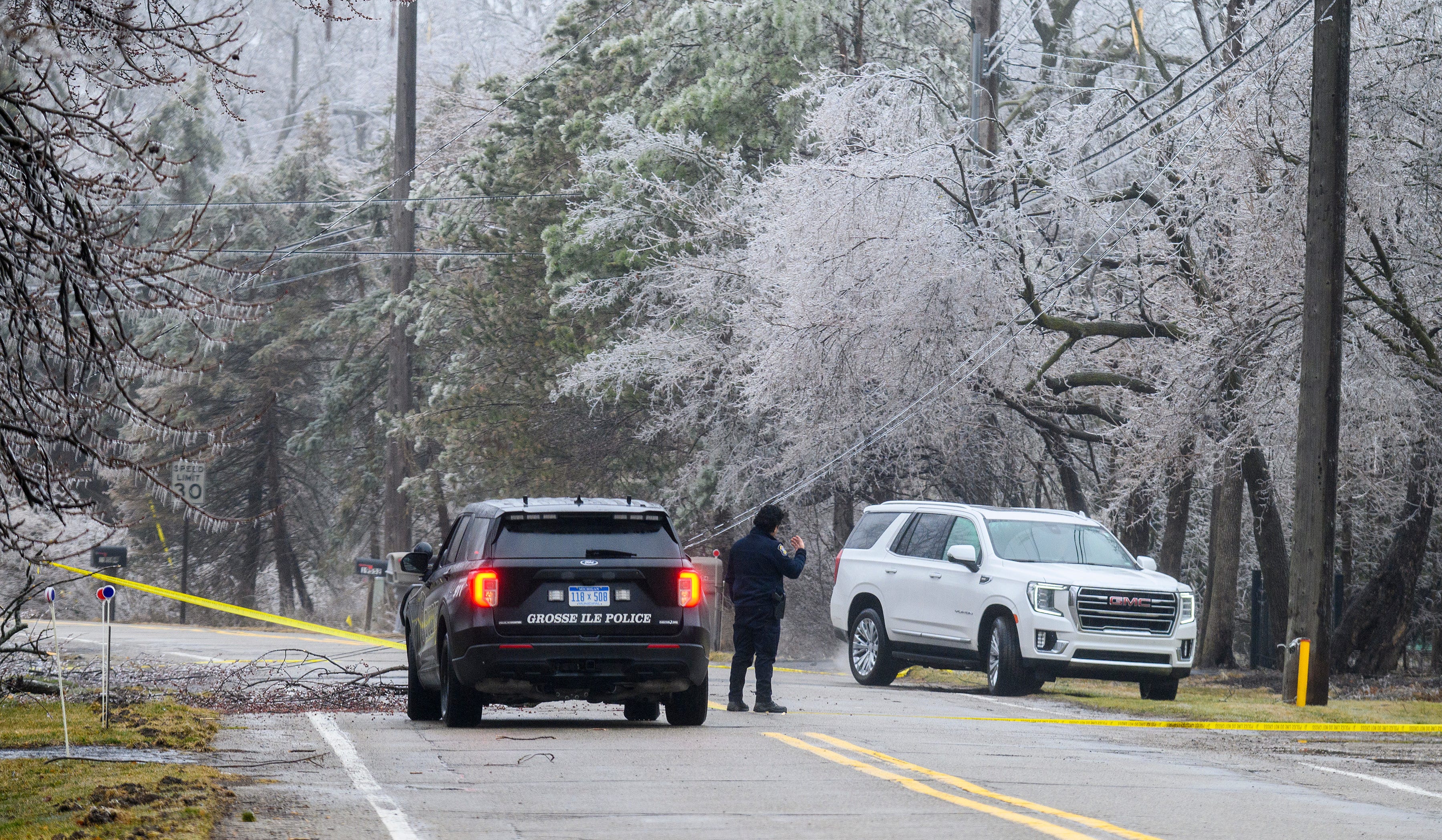 Officer Louis Hurtado of the Grosse Ile Police Department directs a car under a downed secondary power line on Parke Lane on Grosse Ile, Thursday, February 23, 2023.